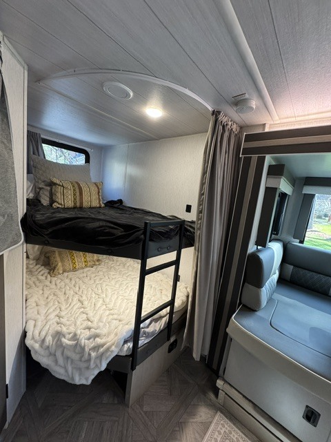 Cozy RV rental interior showcasing modern bunk beds with a ladder, black and white bedding, and a nearby dinette seating area.. Forest River Wildwood X-Lite 2023