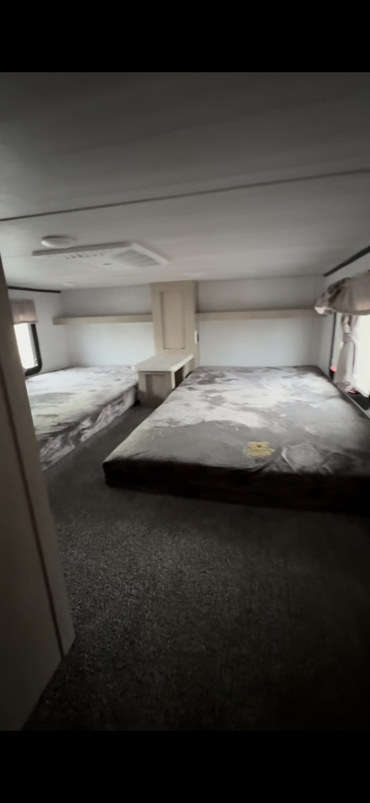 RV rental interior featuring a bunk room with two single beds, a central shared cabinet/table, and grey carpet.. Forest River Wildwood Grand Lodge 2024