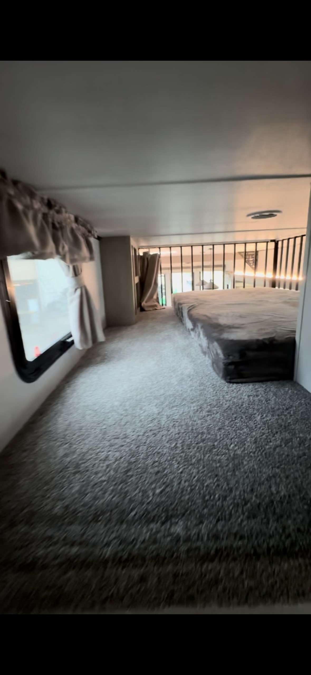 Cozy carpeted RV rental loft sleeping area with a bed, window, and railing overlooking the lower level.. Forest River Wildwood Grand Lodge 2024
