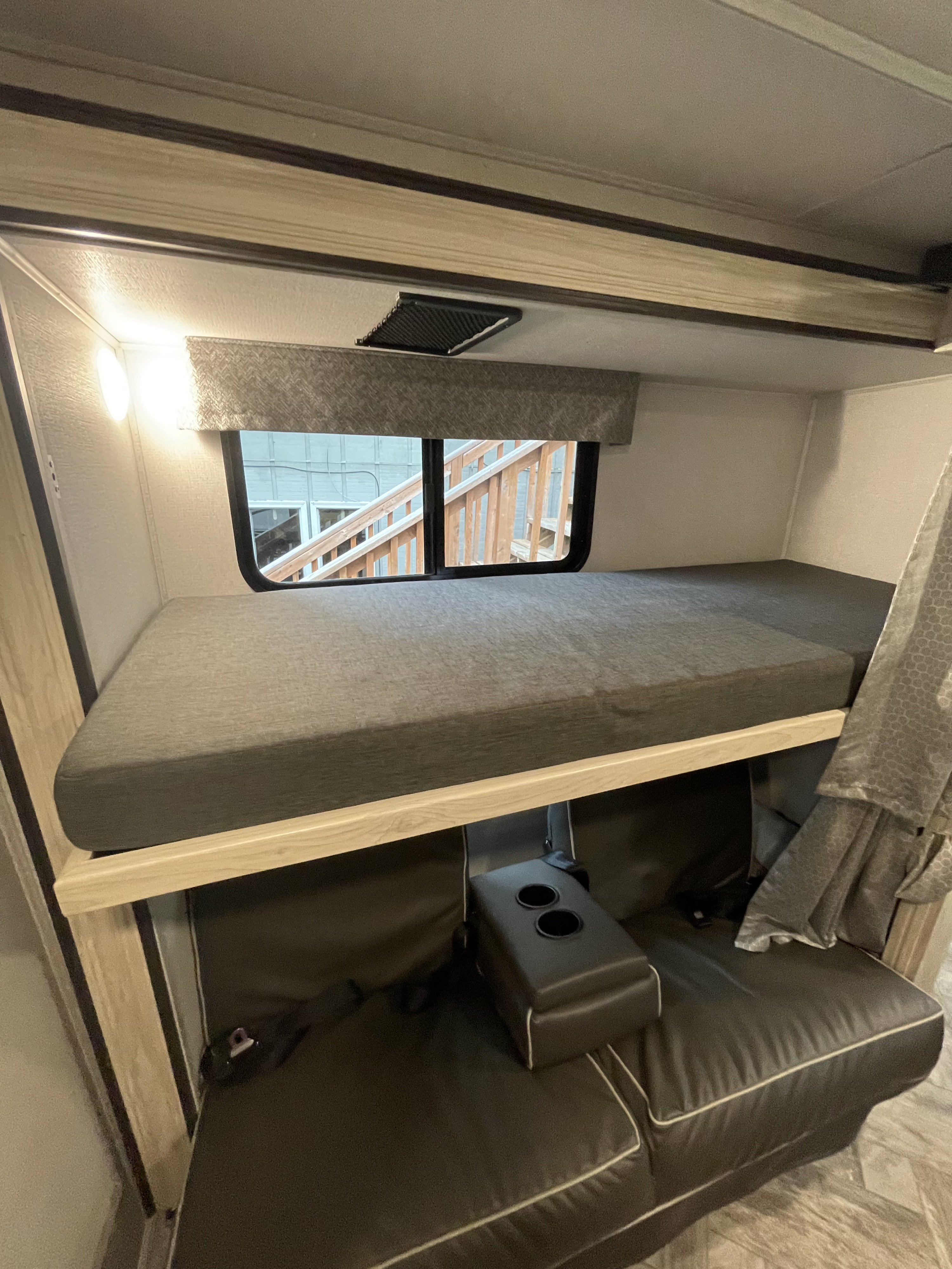 Cozy RV rental bunk bed setup with a lower convertible seating area featuring cup holders, a window, and overhead vent.. Forester LE 2022