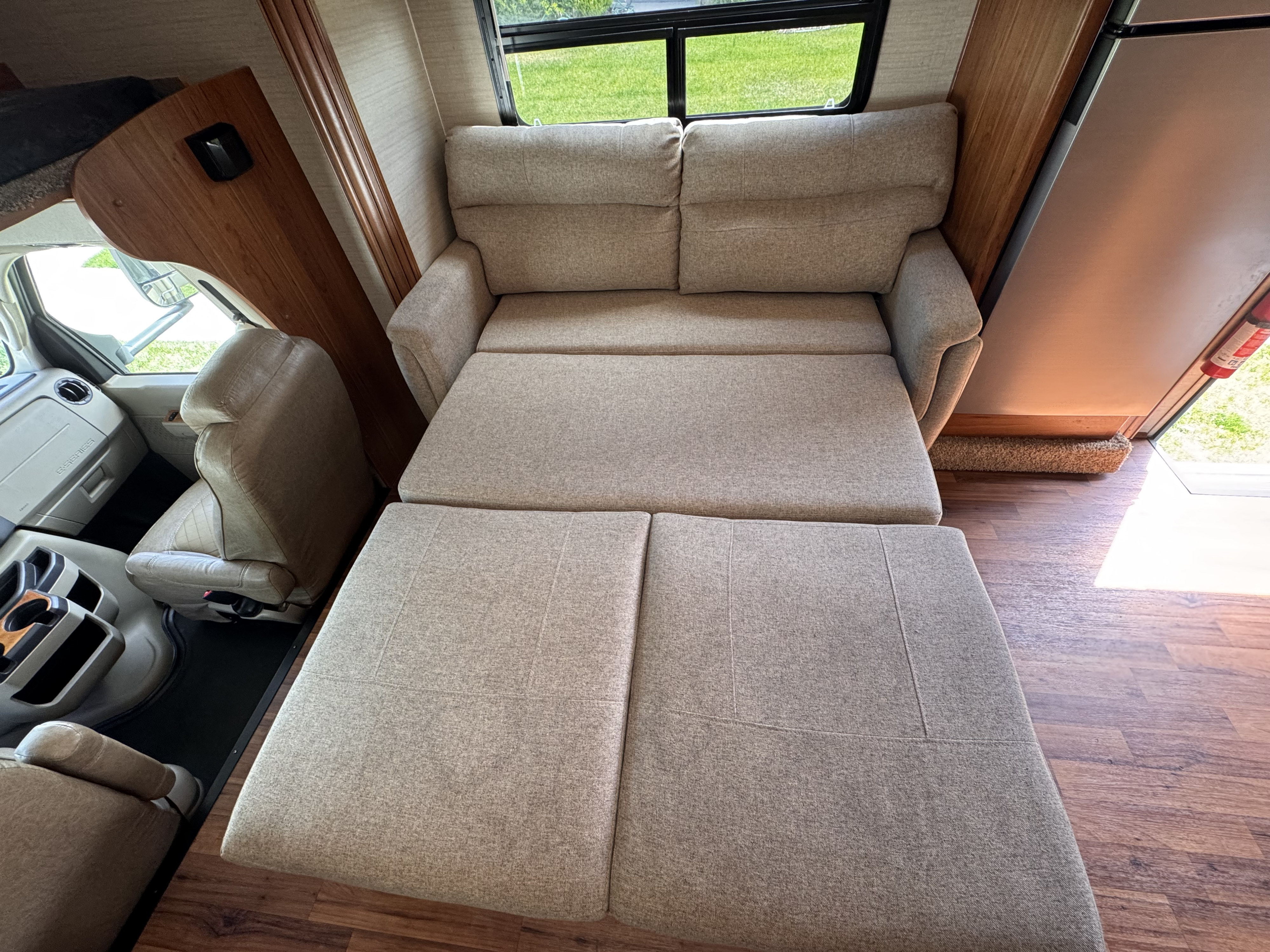 RV rental interior showing an extended sofa bed for sleeping, with driver's cabin and scenic window view.. Jayco Greyhawk 2017