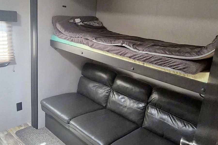 Inside this RV rental, a comfy bunk bed sits above a black leather couch, providing compact sleeping and seating.. Venture Sporttrek 2019