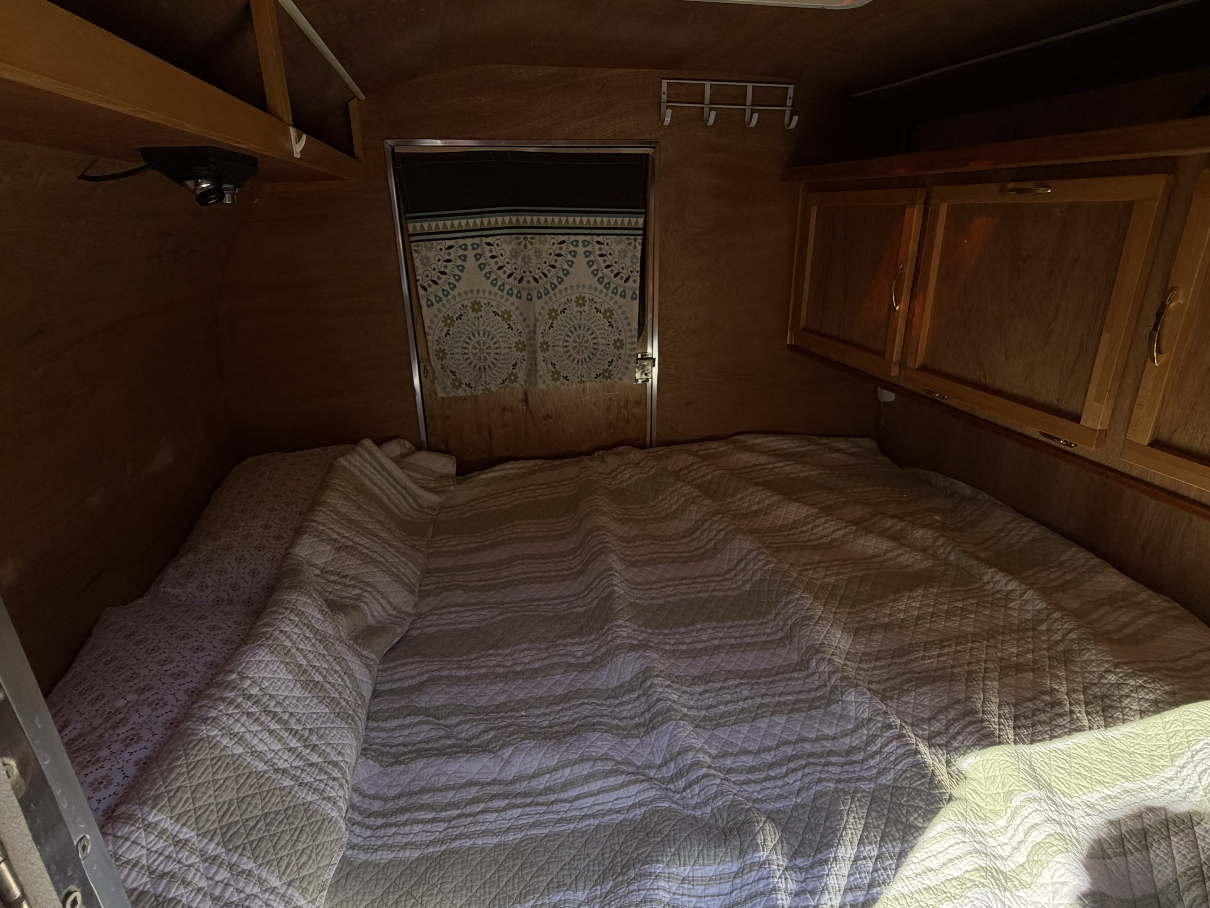 Interior of an rv rental showing a comfortable bed with quilted covers, wooden walls, and storage cabinets. A cozy sleeping area.. UBLT Custom Buid 2008