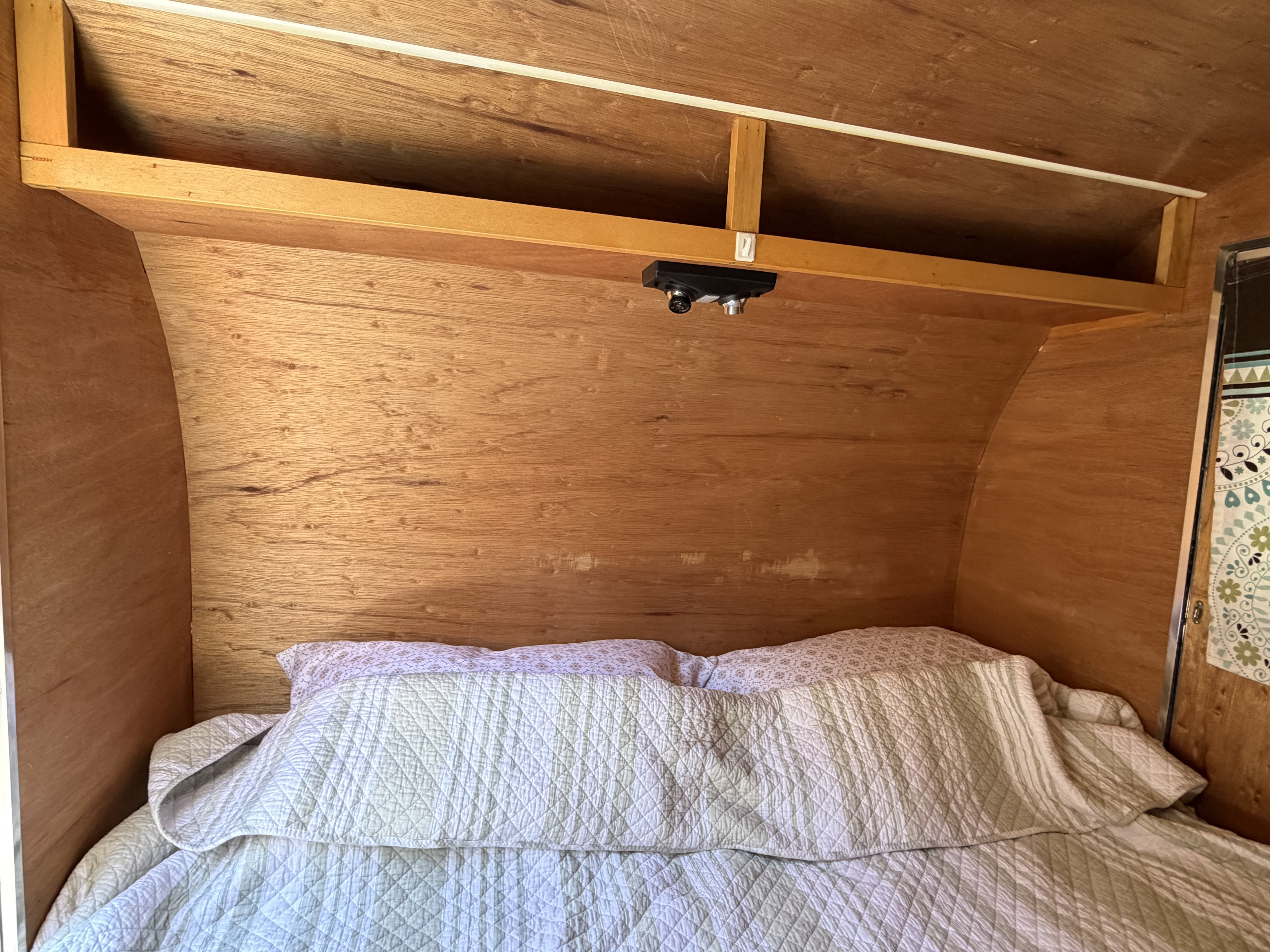 Cozy rv rental sleeping nook with wood-paneled walls, an overhead shelf, and a small ceiling-mounted fixture above the bed.. UBLT Custom Buid 2008