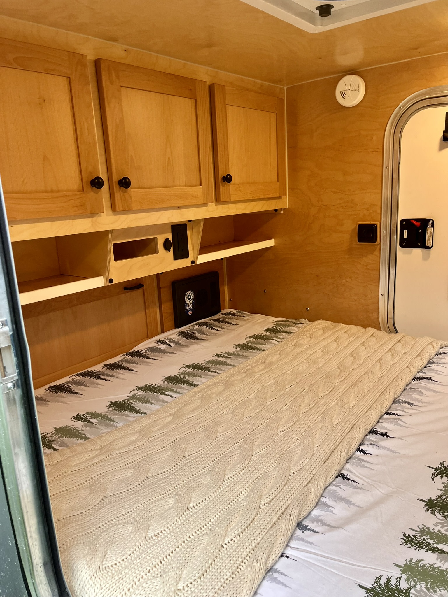 Cozy RV rental interior featuring a comfortable bed with a cable-knit blanket, wooden cabinets, and storage.. Aero Steel 2022
