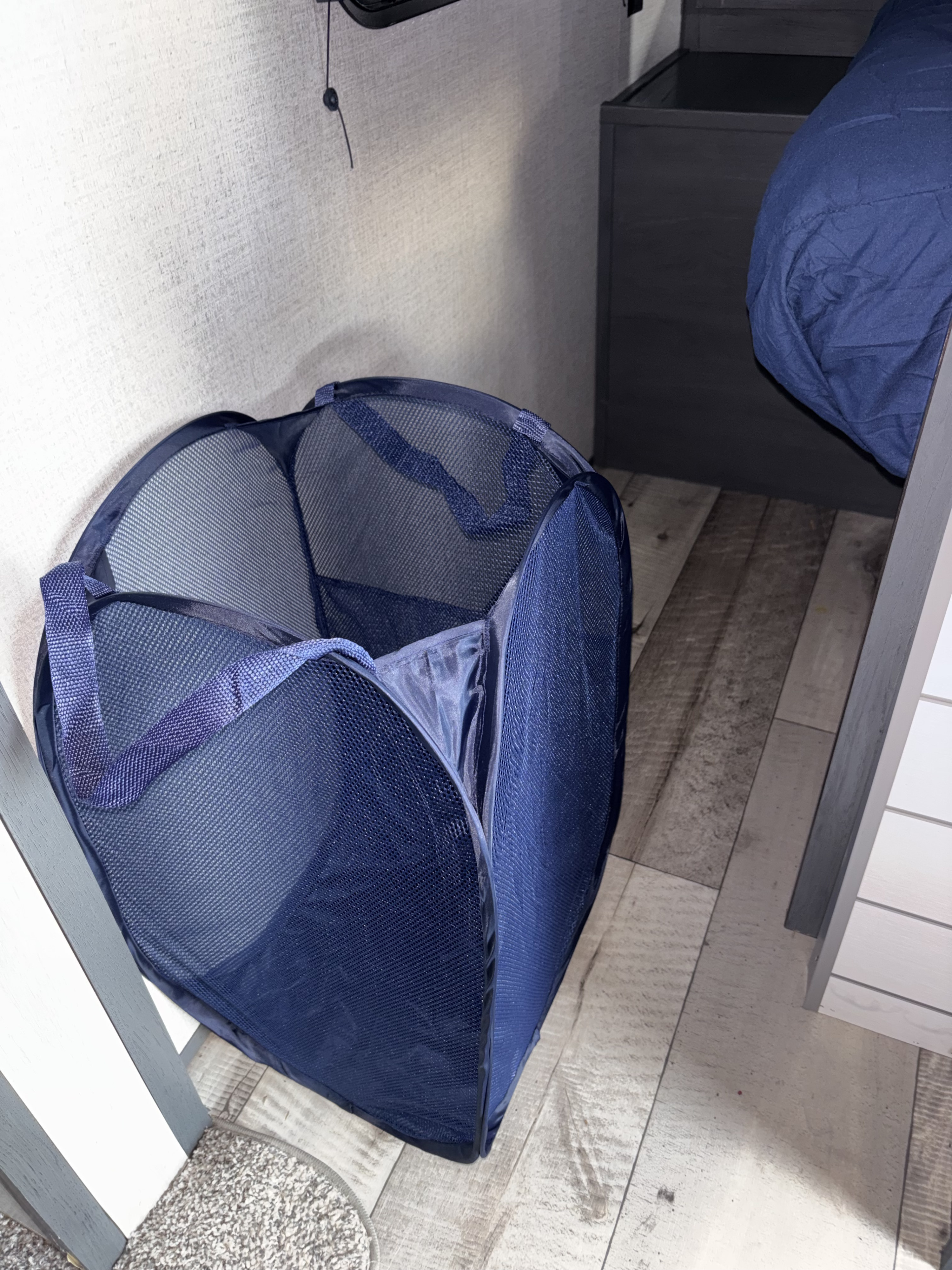 A blue mesh pop-up laundry hamper on wood-look flooring in an RV rental.. Dutchmen Colorado Gold Rush Edition 2021