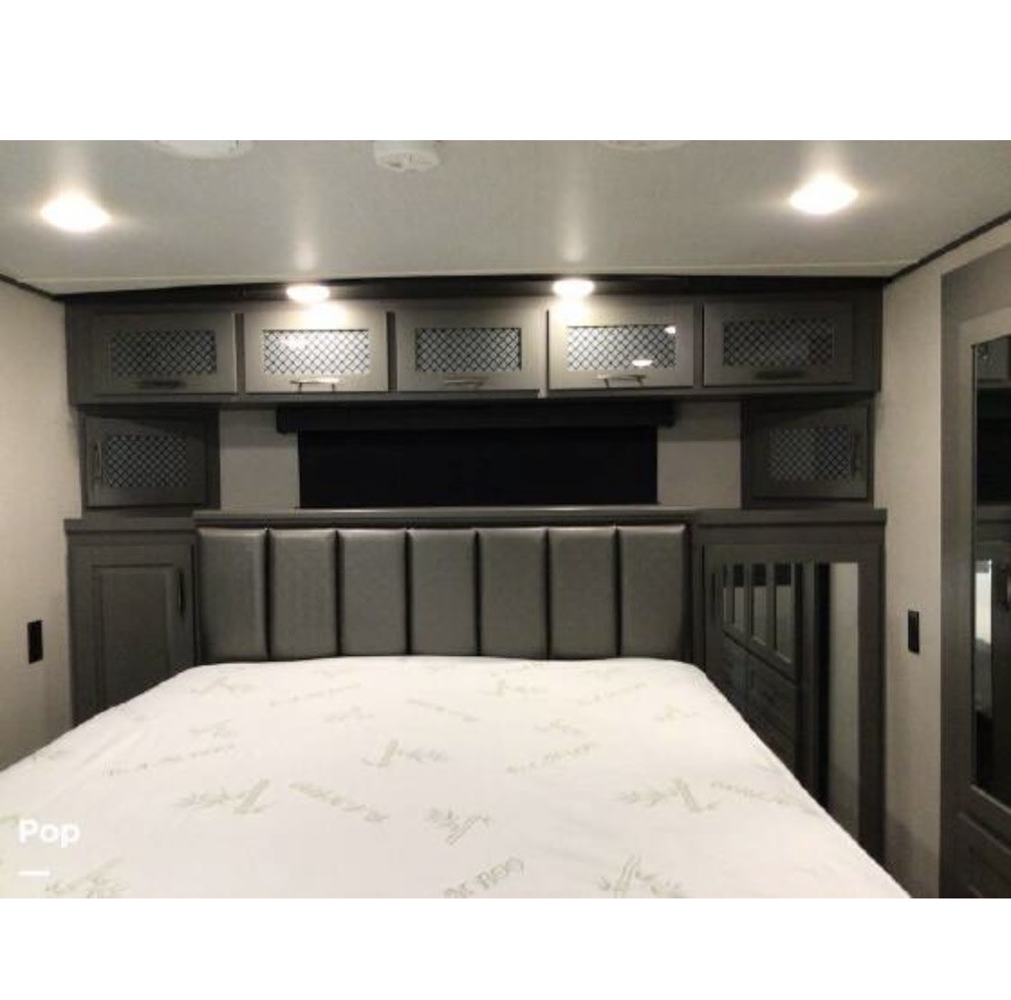 Modern rv rental bedroom featuring a comfy bed, grey padded headboard, and stylish overhead storage cabinets.. Grand Design Momentum 2022