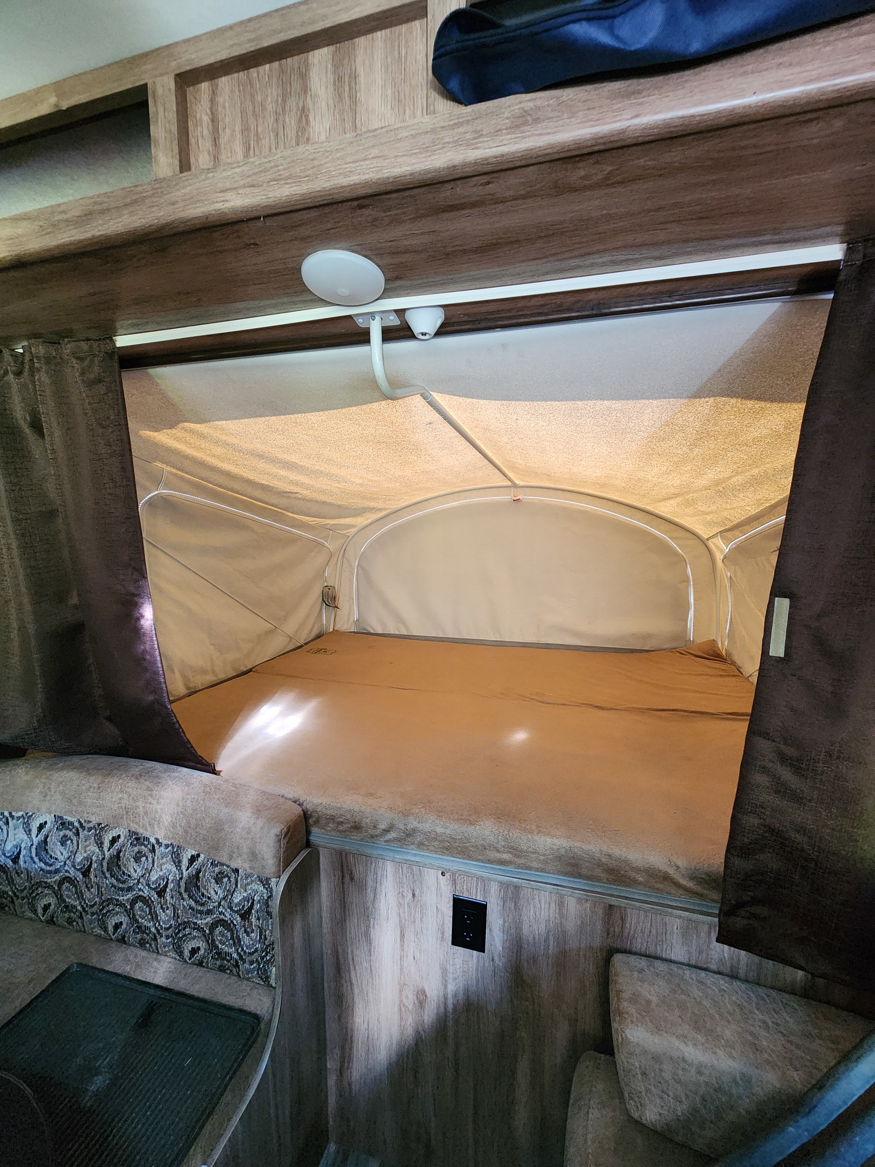 This RV rental features a cozy pop-up bunk bed with canvas walls, side curtains, an overhead light, and a patterned seating area below.. Jayco Jay Feather 2018