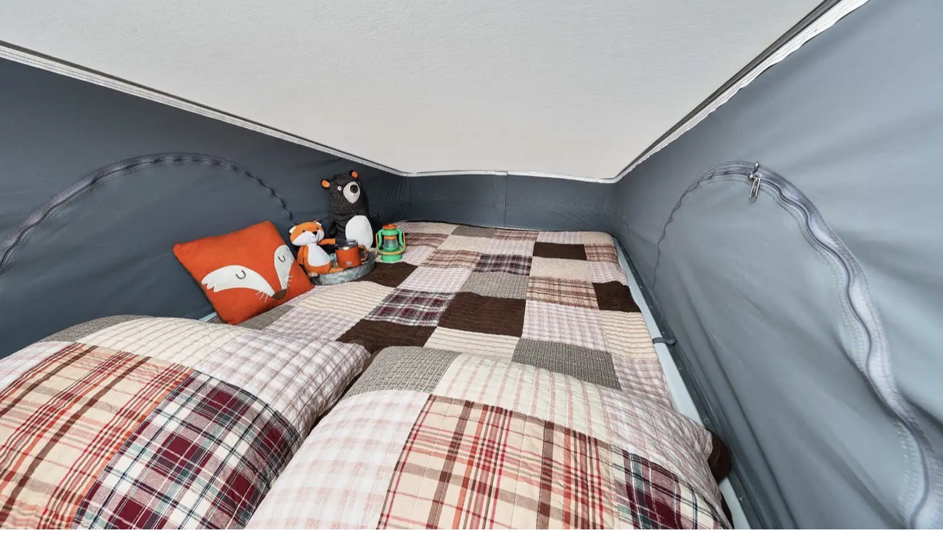 Cozy pop-top sleeping area in an RV rental, featuring patchwork bedding, pillows, and cute stuffed animals for adventure.. Winnebago Solis 59P National Park Fundation 2026