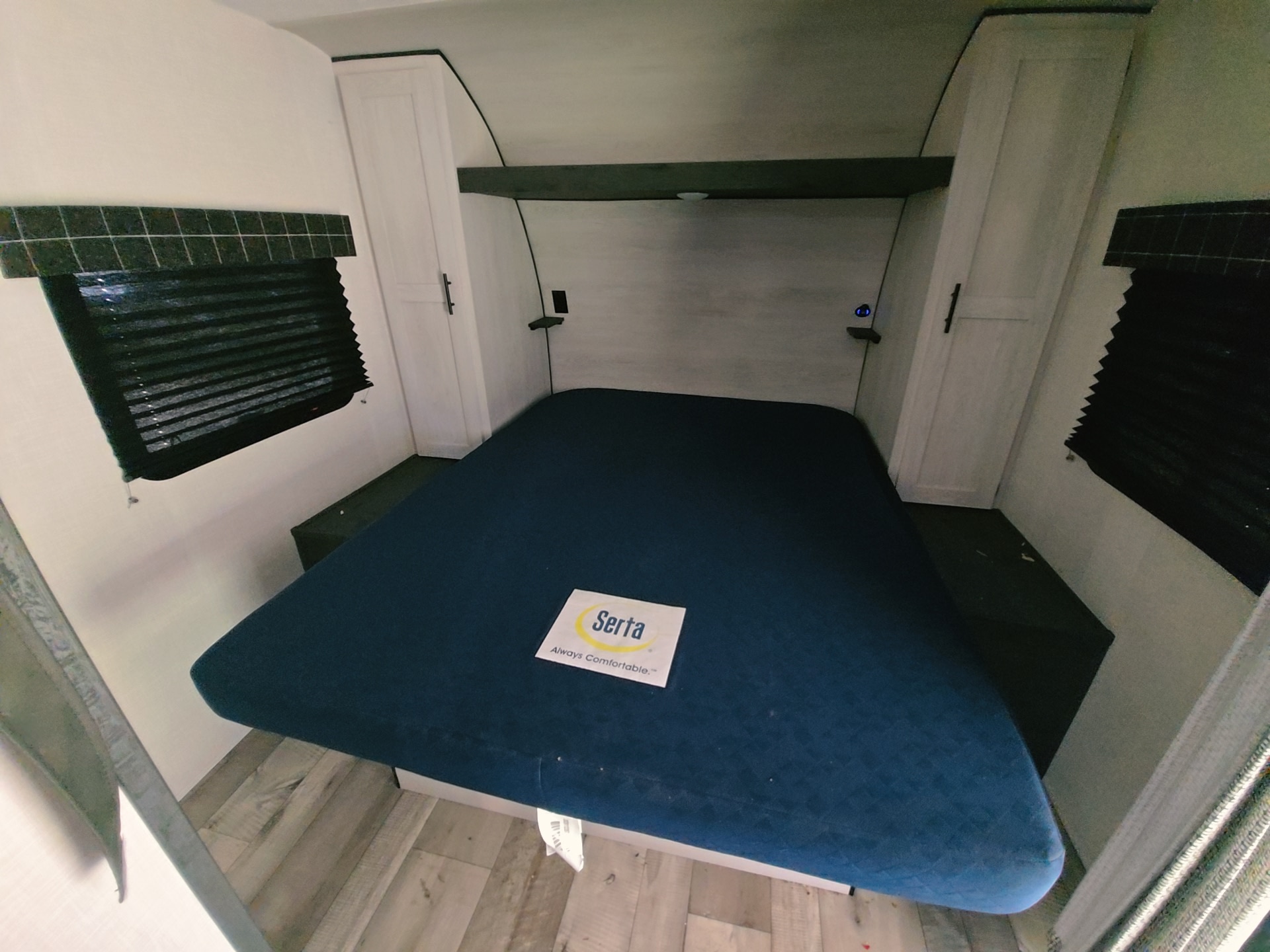 RV rental bedroom featuring a Serta mattress, dark window blinds, side cabinets, and an overhead shelf.. KZ RV sportsman 2022