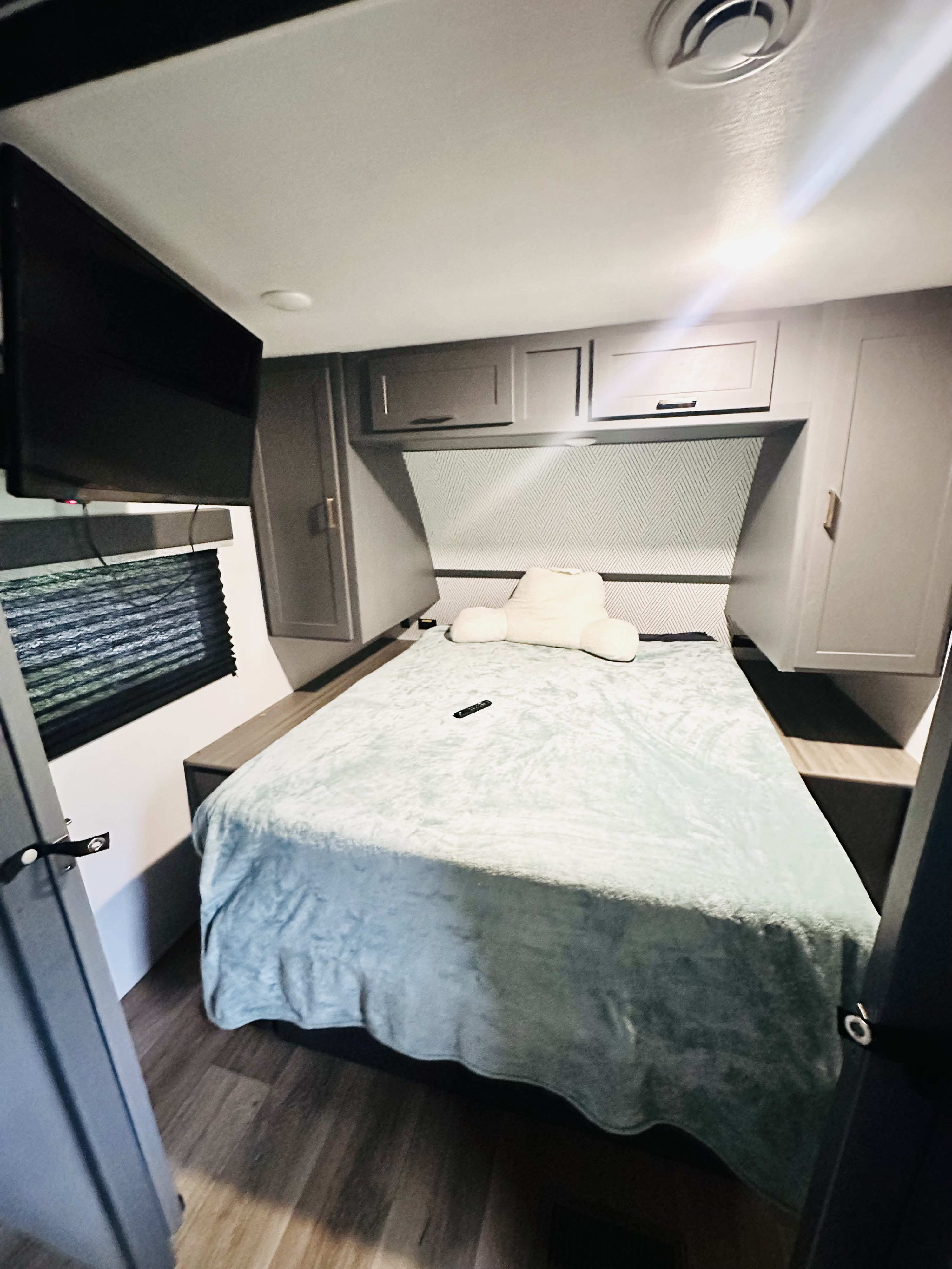 Cozy RV rental bedroom featuring a light blue bed, mounted TV, and practical overhead storage cabinets.. Keystone RV Bullet Crossfire 2024
