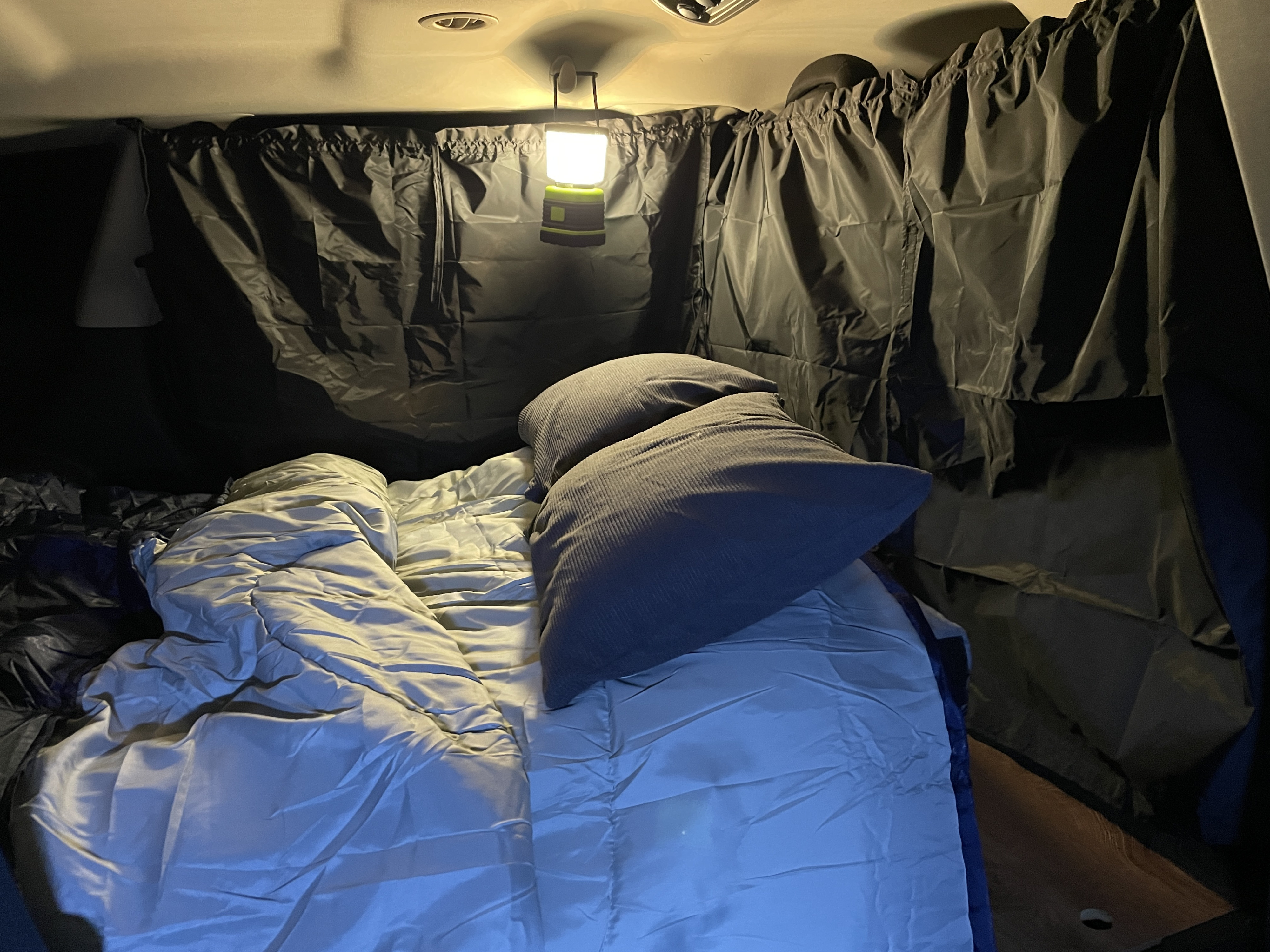 Cozy RV rental sleeping setup with privacy curtains and a bright lantern, ideal for car camping adventures.. Dodge Journey 2016