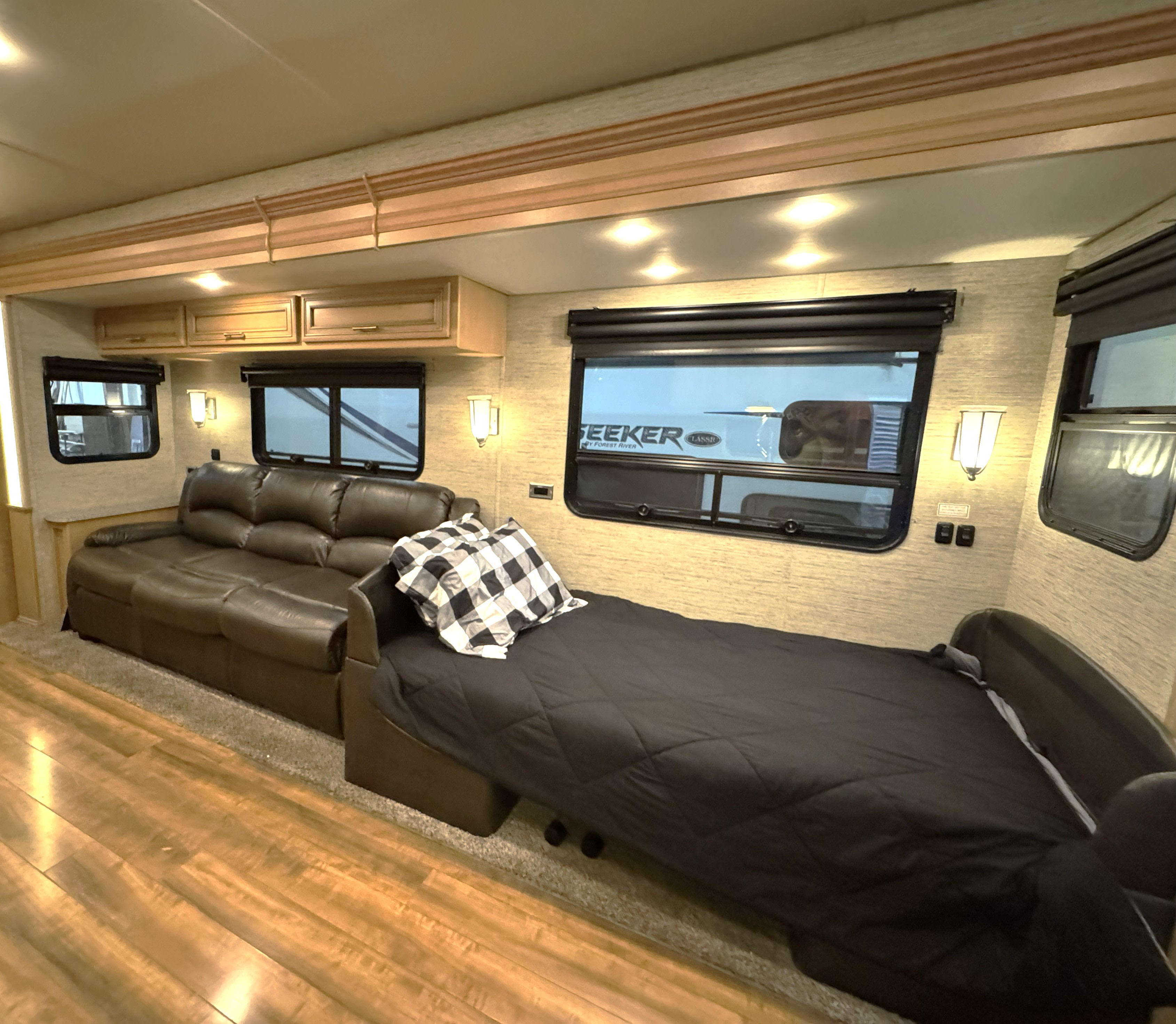Bright rv rental interior: brown leather sofa, extended pull-out bed with black comforter, wall sconces, wood & carpet flooring.. Newmar Canyon Star 2016