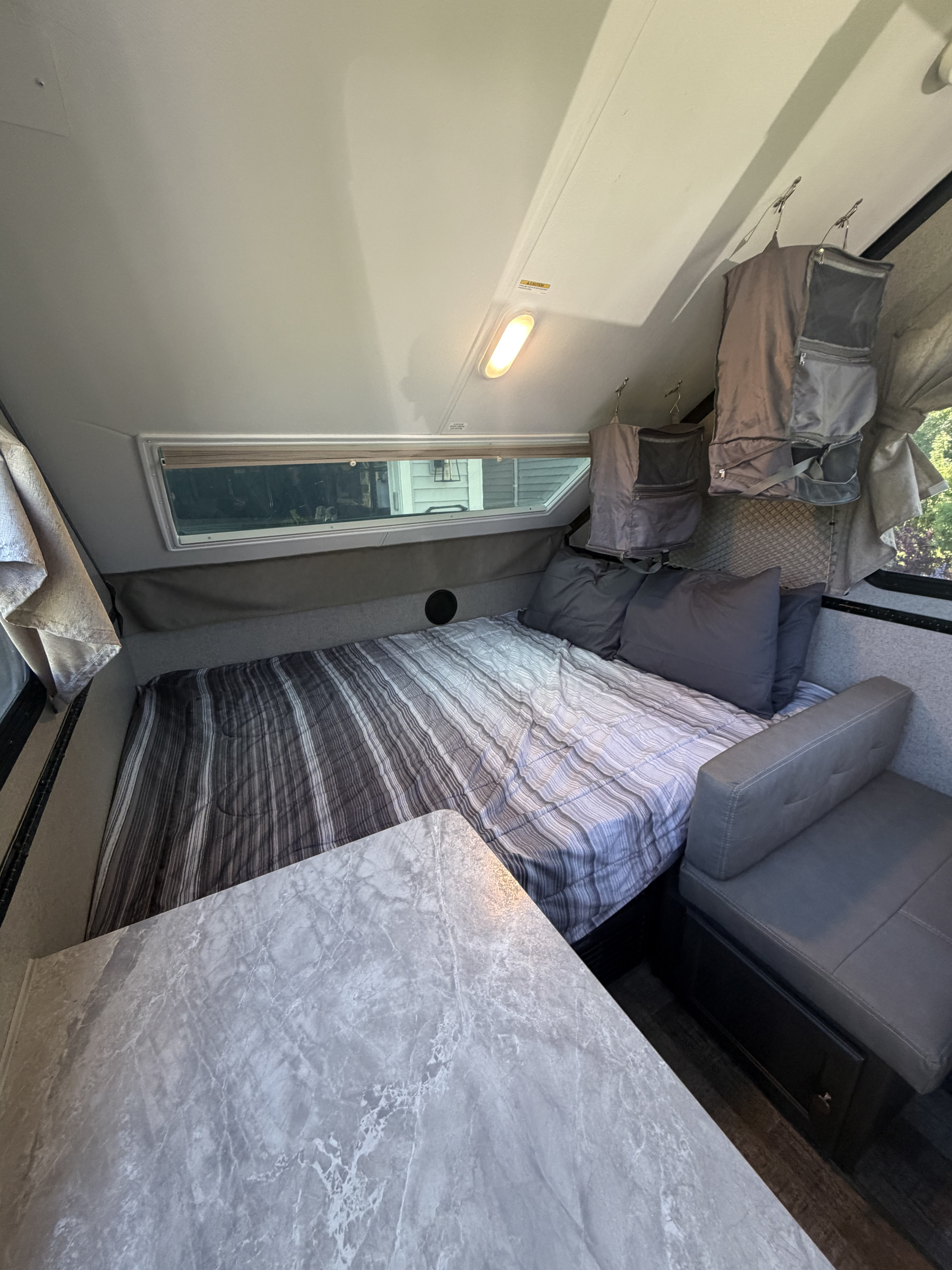 Cozy RV rental interior featuring a striped bed, marble-top dinette, bench seating, and hanging storage. Ideal for road trips.. Forest River Rockwood Premier 2021