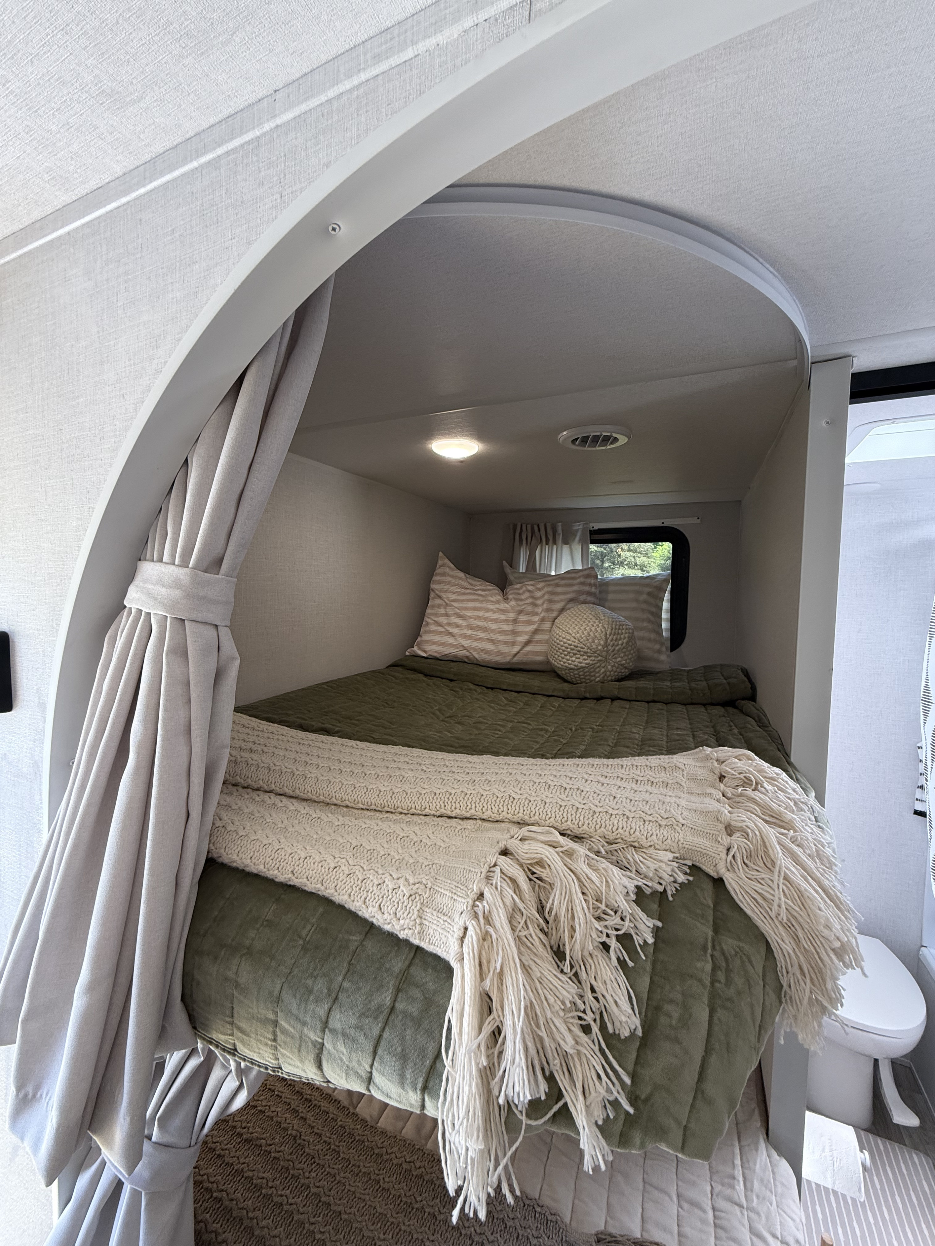 Cozy RV rental bunk bed featuring a green comforter, knitted throw, and patterned pillows for comfortable travel.. Forest River Wildwood X-Lite 2026