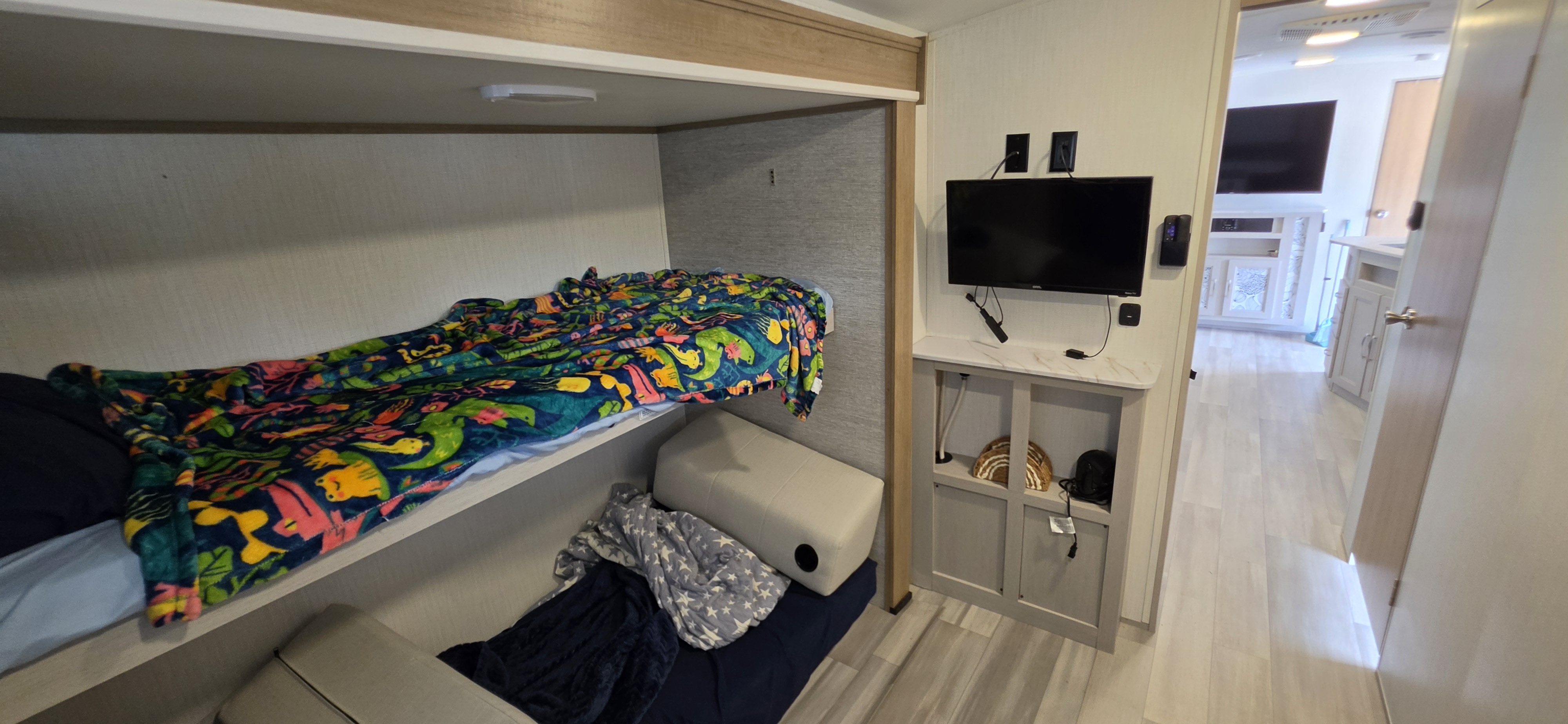 RV rental sleeping area with bright bunk beds, a wall-mounted TV, and a view into the hallway.. Cruiser RV Embrace 2024