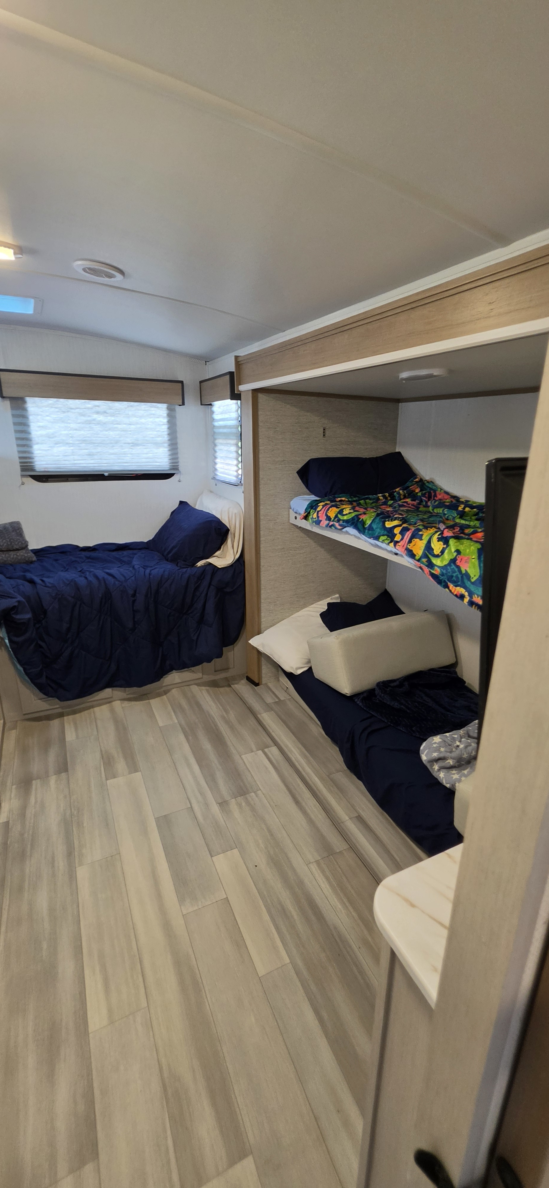 RV rental bedroom with a bed and bunk beds. Features light wood flooring and bright interior lighting.. Cruiser RV Embrace 2024