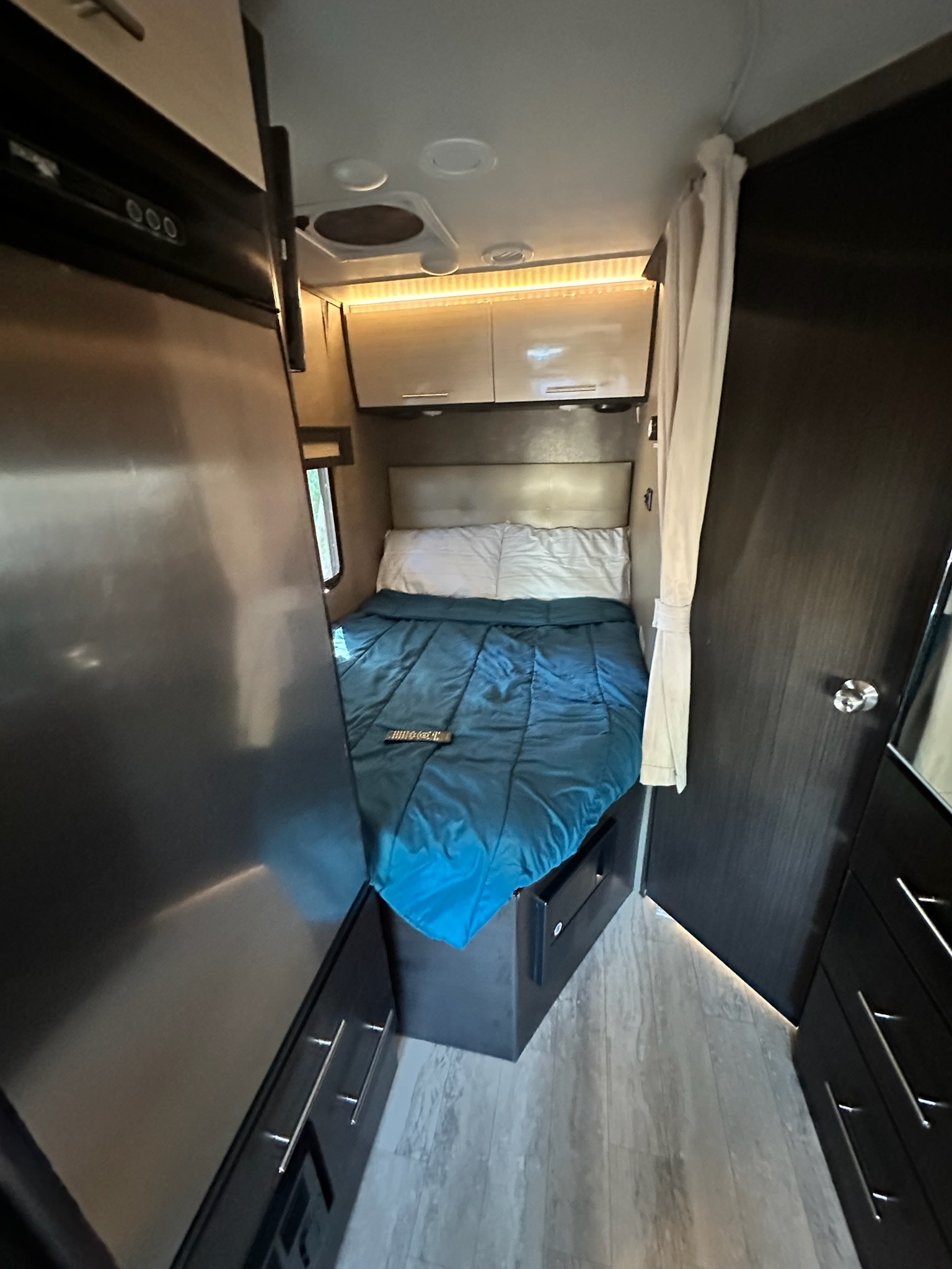 Experience comfort in this rv rental bedroom: a cozy bed, overhead lighting, fridge, and storage cabinets in a compact space.. THMC Gemini 23TK (So.Cal.) 2017