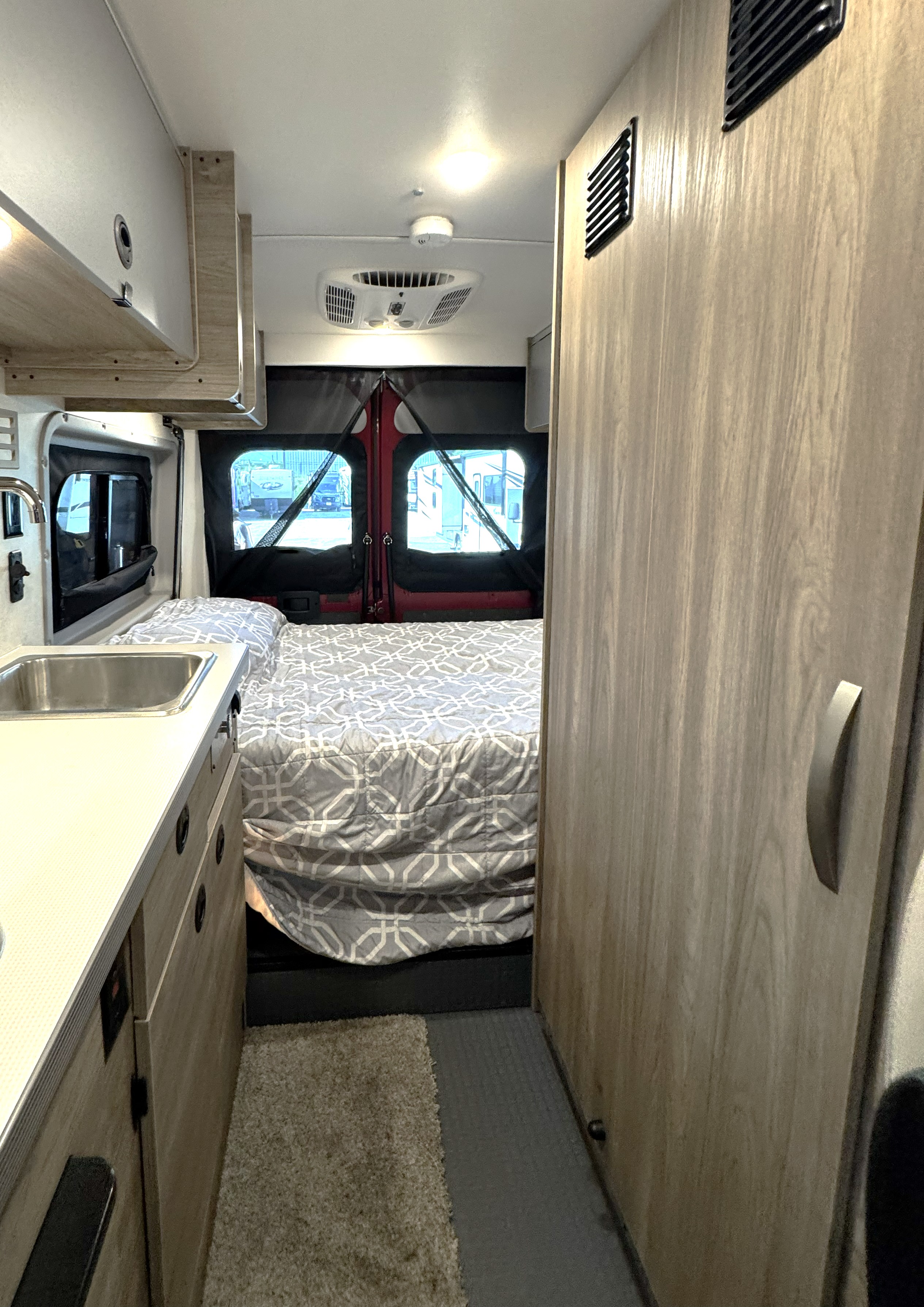 RV rental interior with a compact bedroom, kitchenette sink, and wooden storage cabinetry, ideal for travelers.. Winnebago Solis 2023