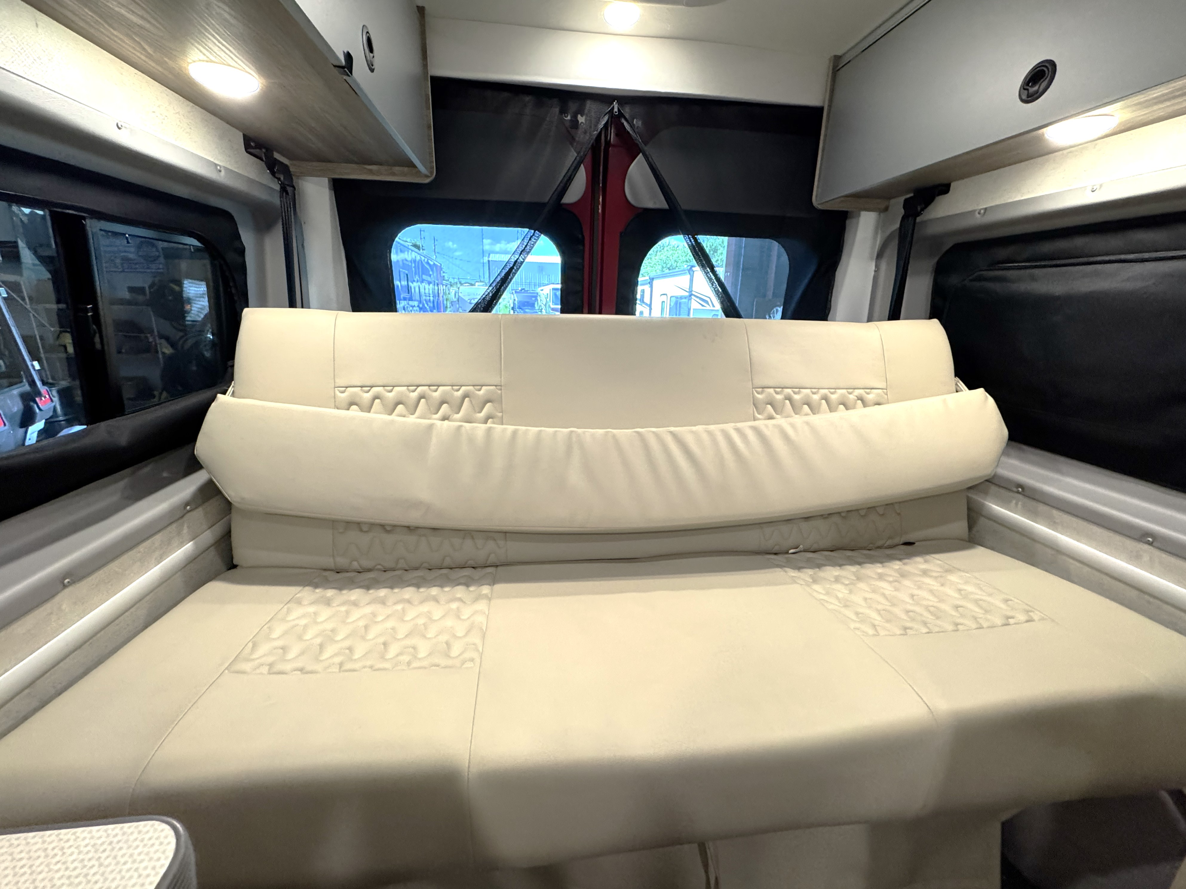 This RV rental interior features a versatile cream-colored modular couch/bed with quilted accents, overhead storage, and rear windows.. Winnebago Solis 2023
