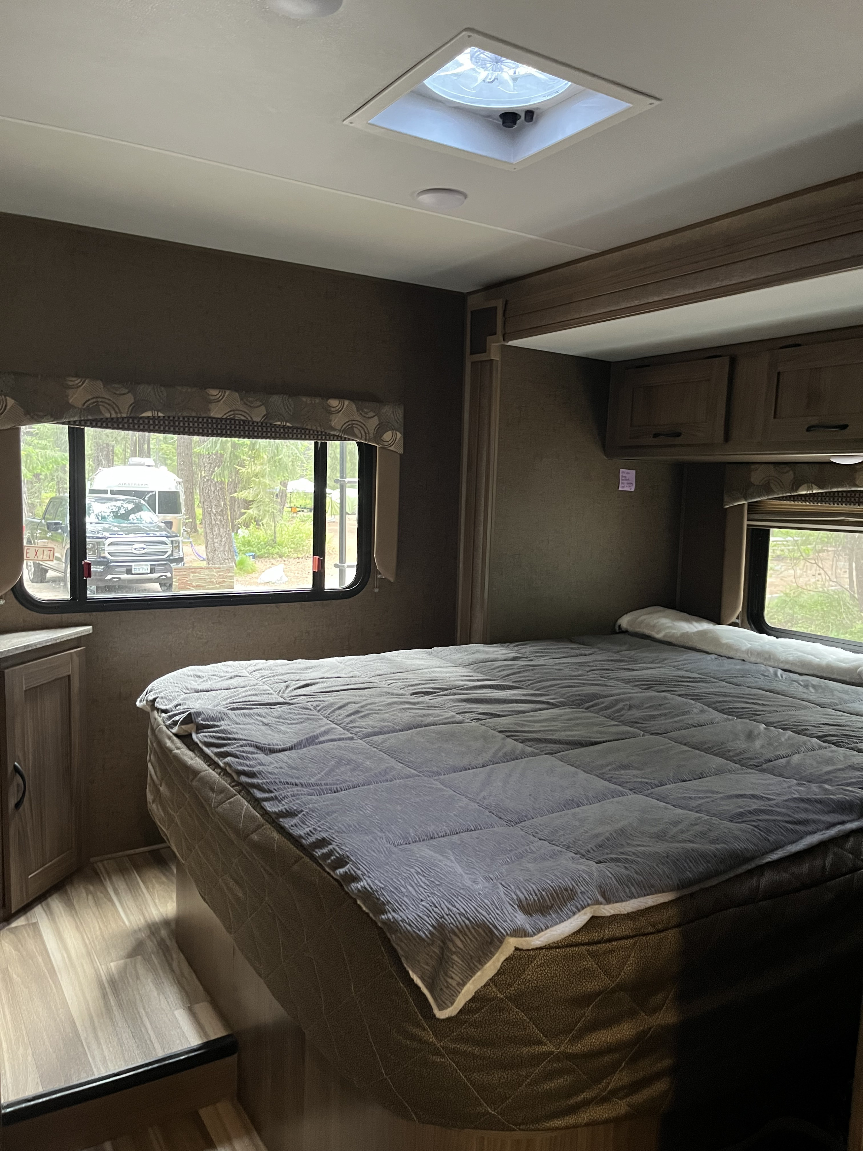 Cozy rv rental bedroom featuring a large bed, overhead cabinets, ceiling vent, and a window view of a campsite.. Forest River Coachmen Freelander 2017