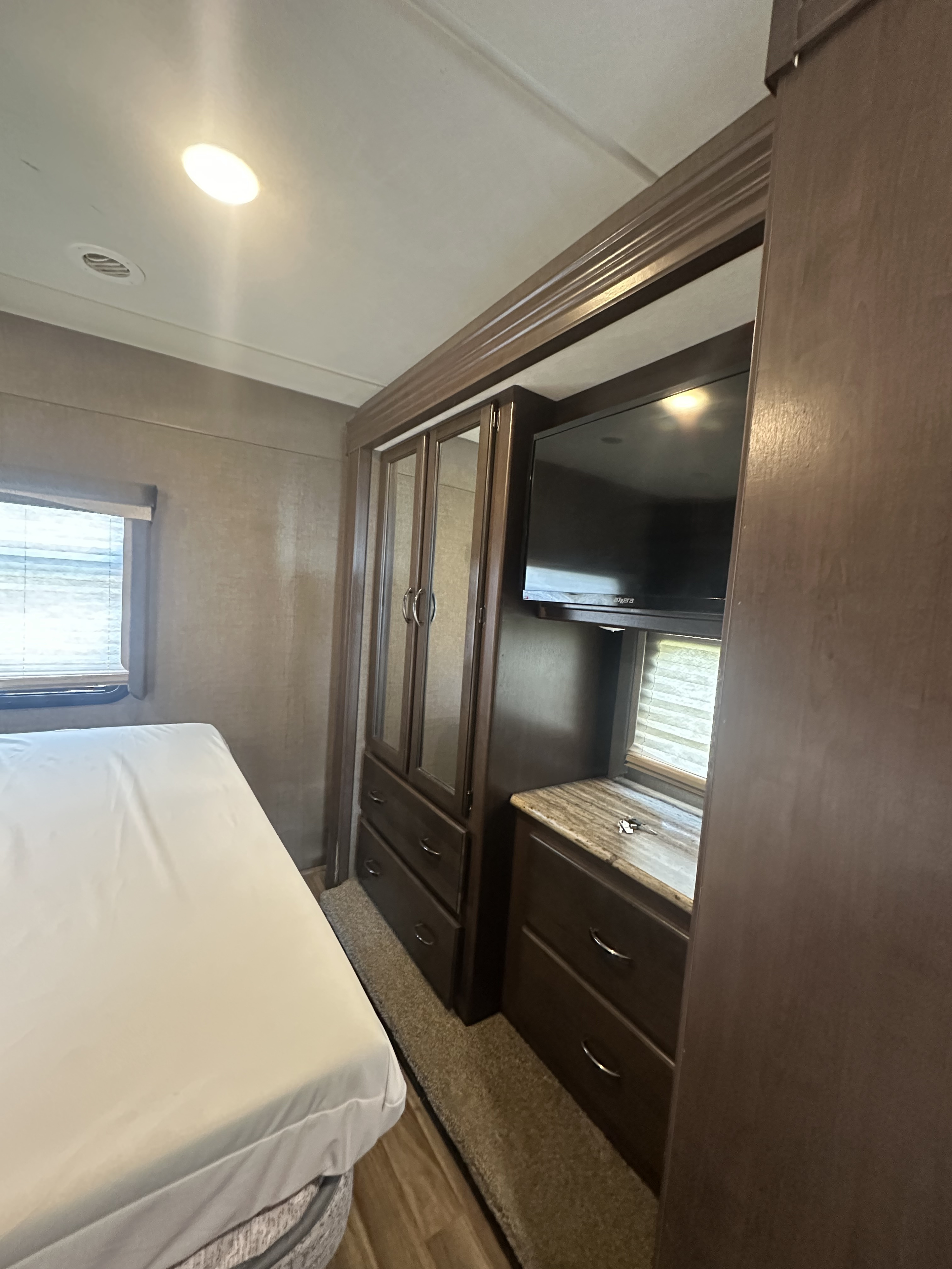Inside this RV rental bedroom: a comfy bed, wardrobe with mirrored doors, TV, and window with blinds.. Thor A.C.E. 2018