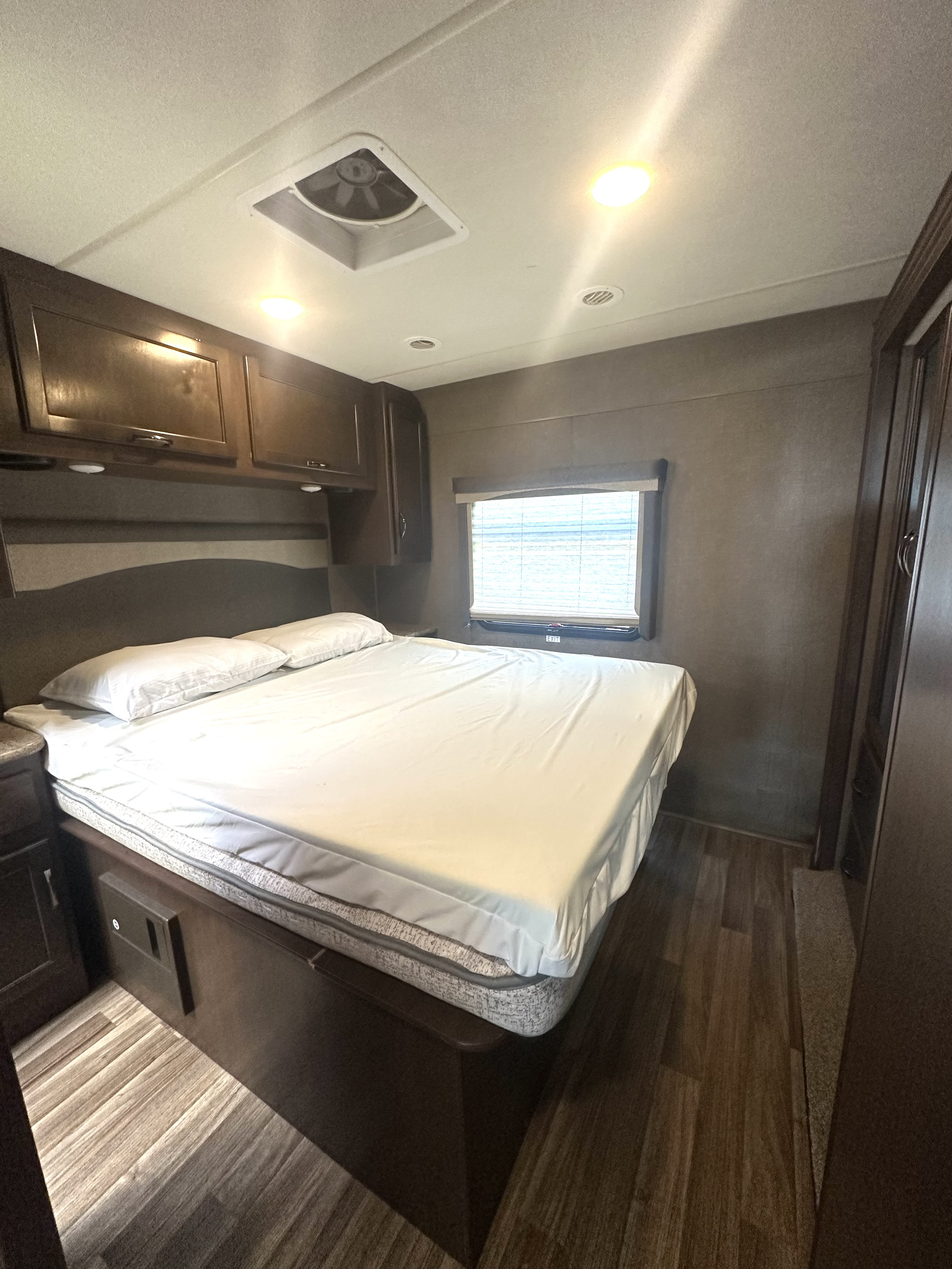 RV rental bedroom: a compact space with a bed, dark wood cabinets, window with blinds, and ceiling lights, ideal for travelers.. Thor A.C.E. 2018