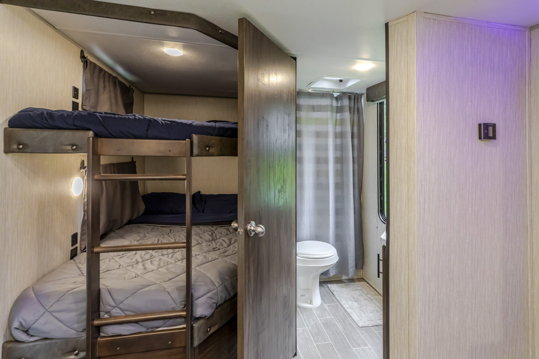 Inside an RV rental: cozy bunk beds with a ladder, adjacent to a compact bathroom with a toilet and shower.. Forest River Cherokee 2020