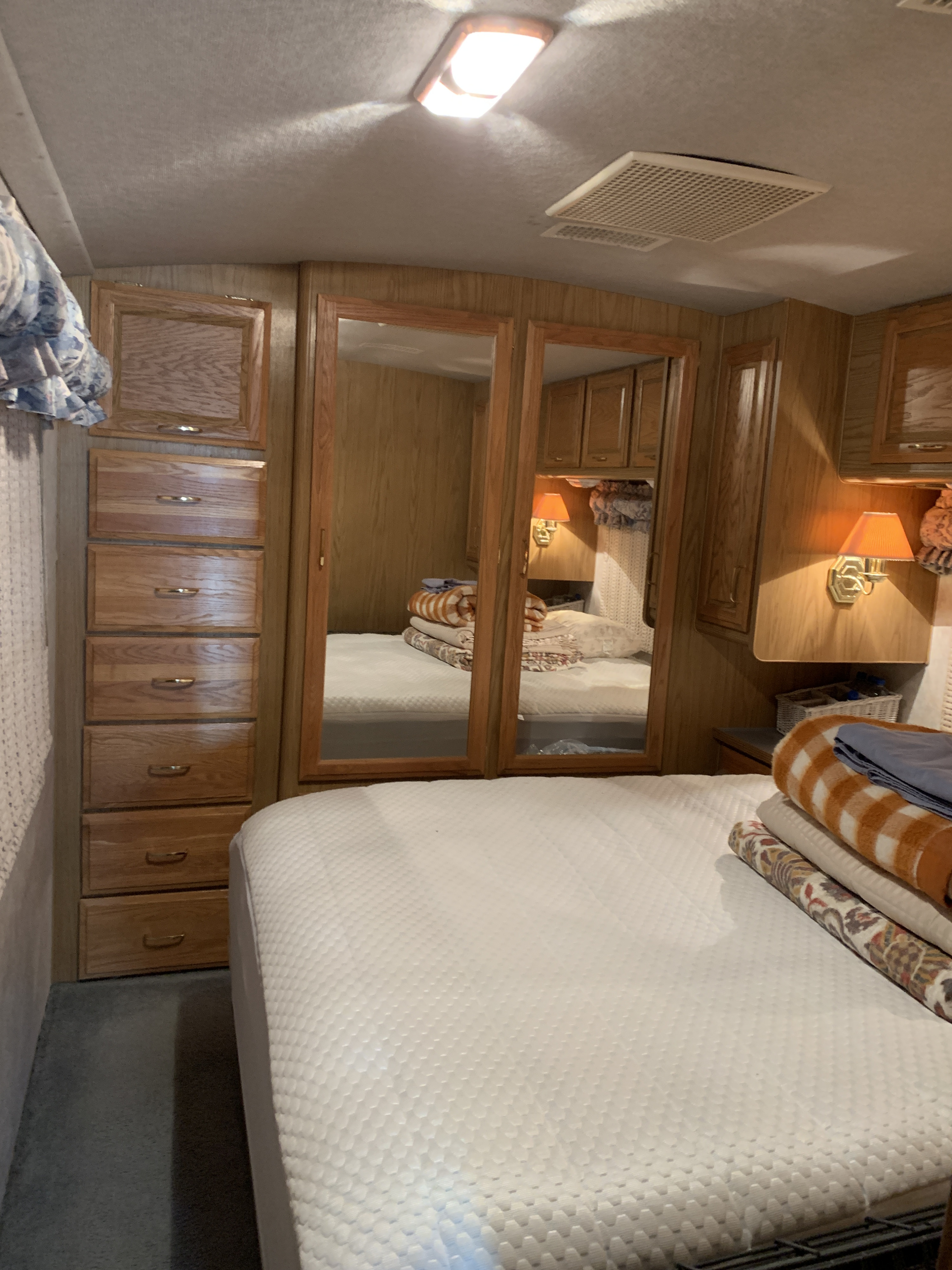 Cozy RV rental bedroom with a comfortable bed, wood storage, mirrored closets, and warm lighting. Ideal for your next trip.. Fleetwood Bounder 1997