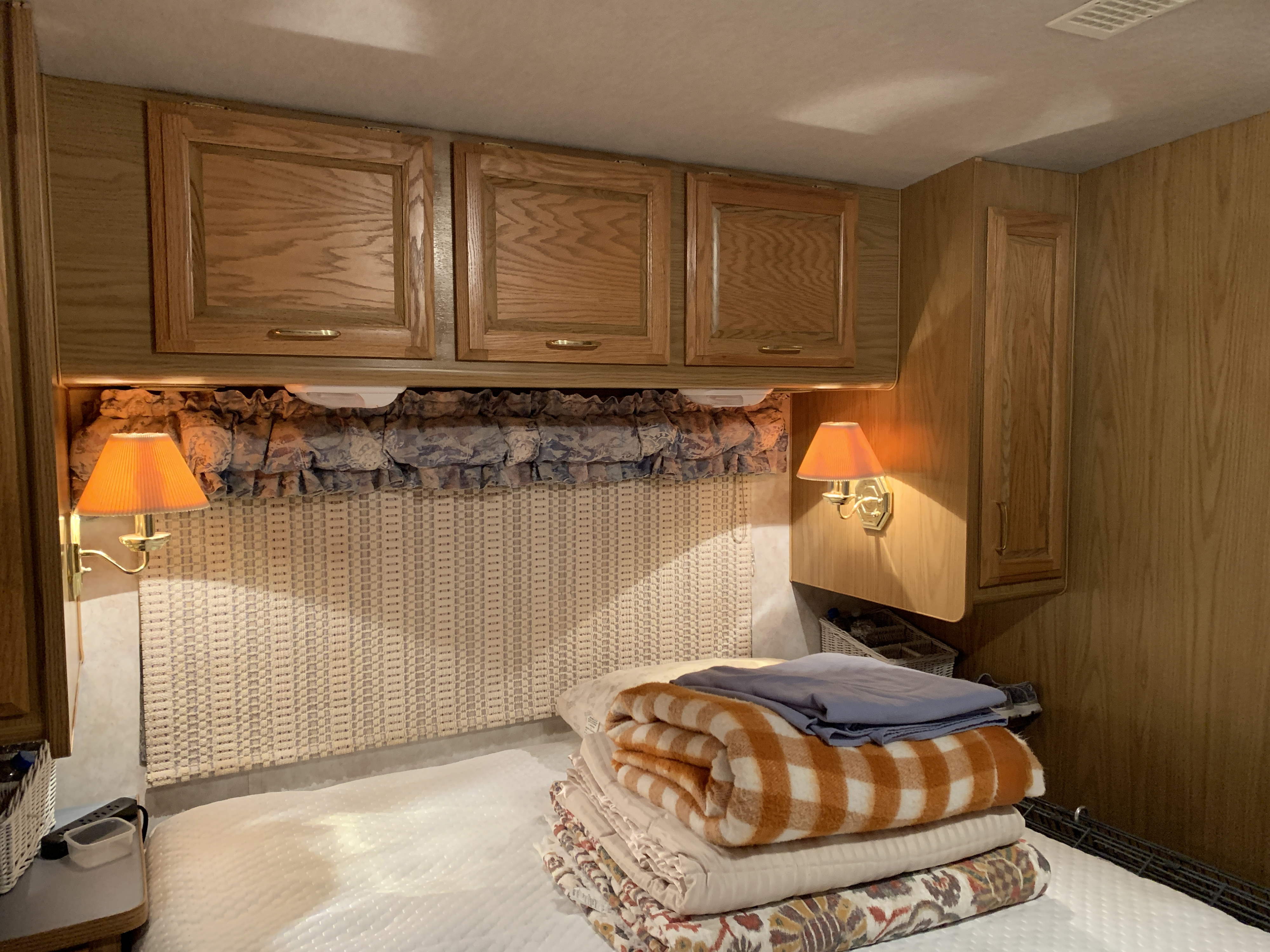 Cozy RV rental bedroom with warm lighting, wooden cabinets, and comfortable blankets, ideal for travel.. Fleetwood Bounder 1997