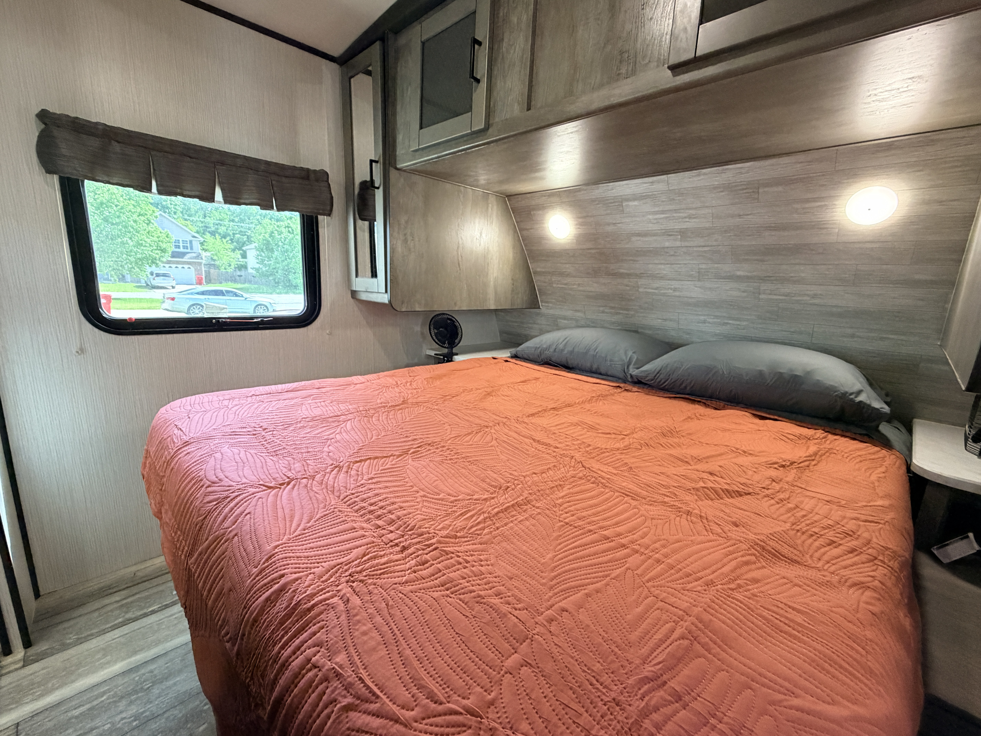 Cozy RV rental bedroom features a quilted bed, window with a view, and convenient overhead storage.. Heartland RVs North Trail 2020