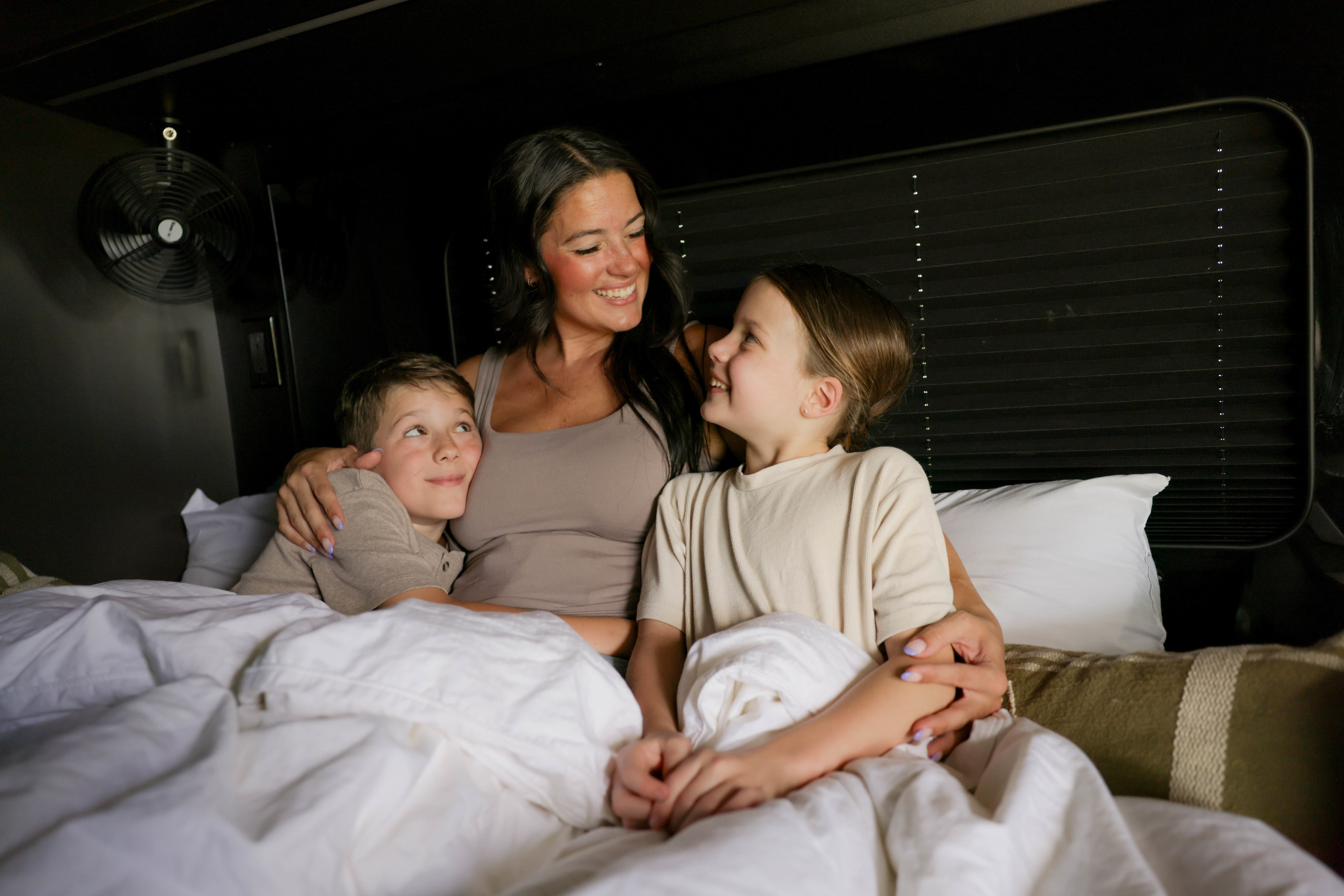 Cozy family time in an RV rental bed! A mother and her children snuggle, sharing smiles during their travel adventure.. 27North 27North Class B 2024
