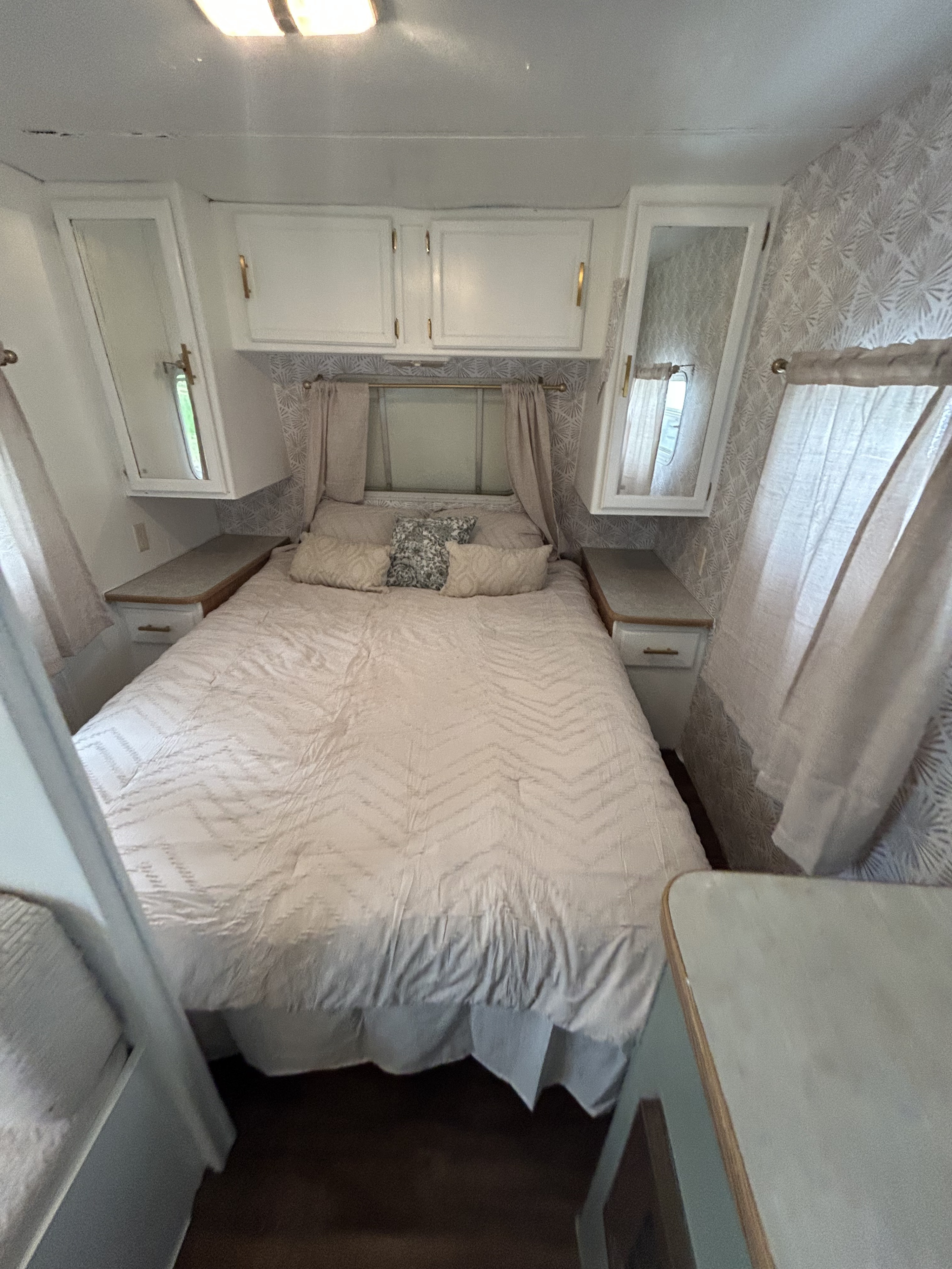 This comfy RV rental bedroom features a bed with quilted bedding, overhead cabinets, side tables, and decorative wallpaper.. Century-Skyline Century-Skyline Trailer 2003