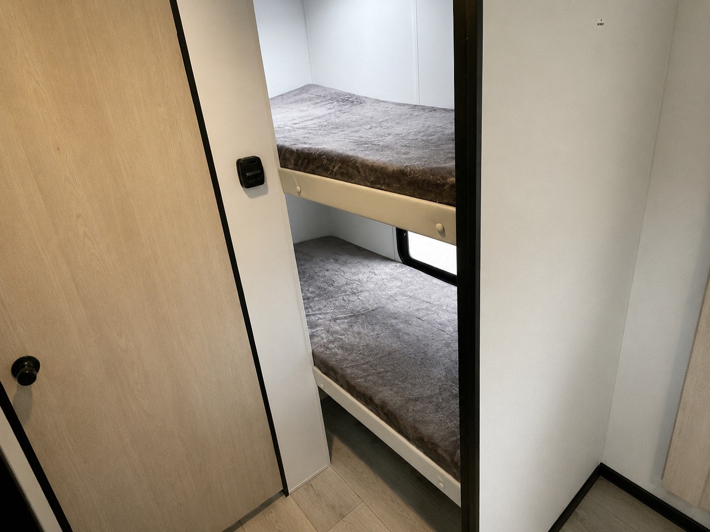 RV rental interior view: two bunk beds with grey bedding visible behind a light wood door. Ideal for family adventures.. Forest River Avenger 2025