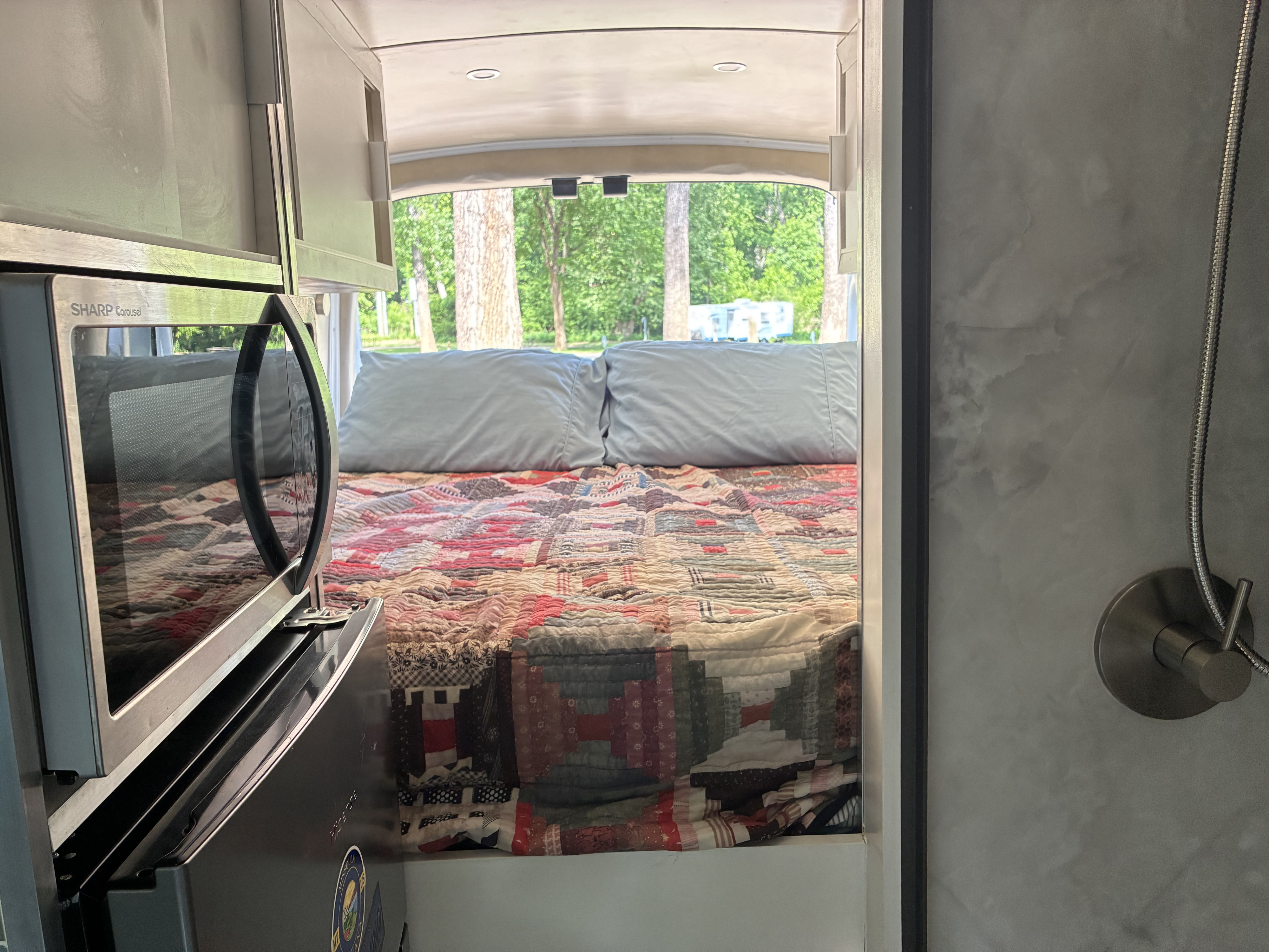 Explore this rv rental interior: a cozy bed with quilt, microwave, and a shower corner, set for relaxing road trips.. Ford F350 2019
