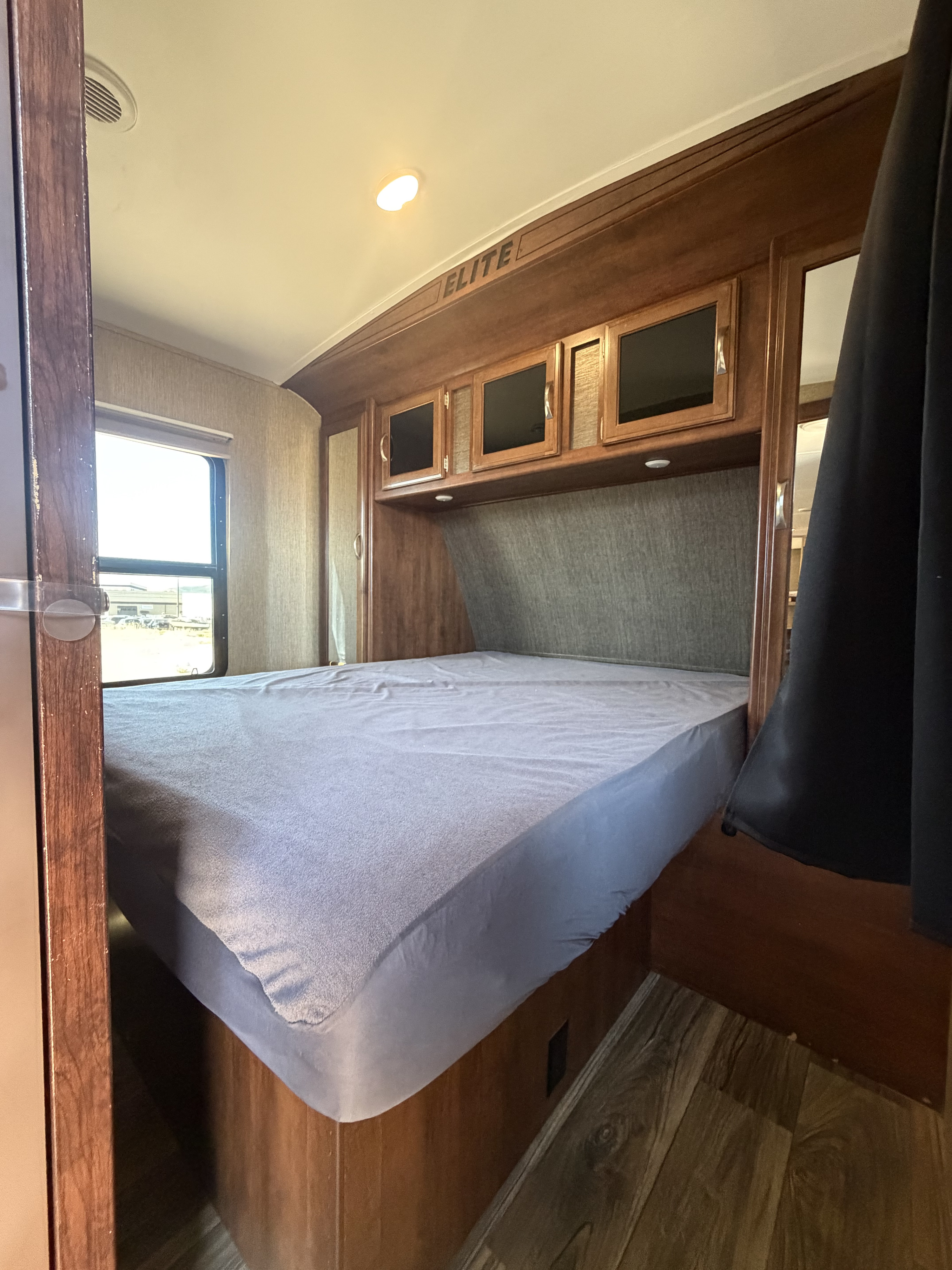 Inside an RV rental bedroom: cozy bed with overhead storage, wood accents, window, and "ELITE" branding. Ideal for travel.. Keystone RV Passport Elite 2016