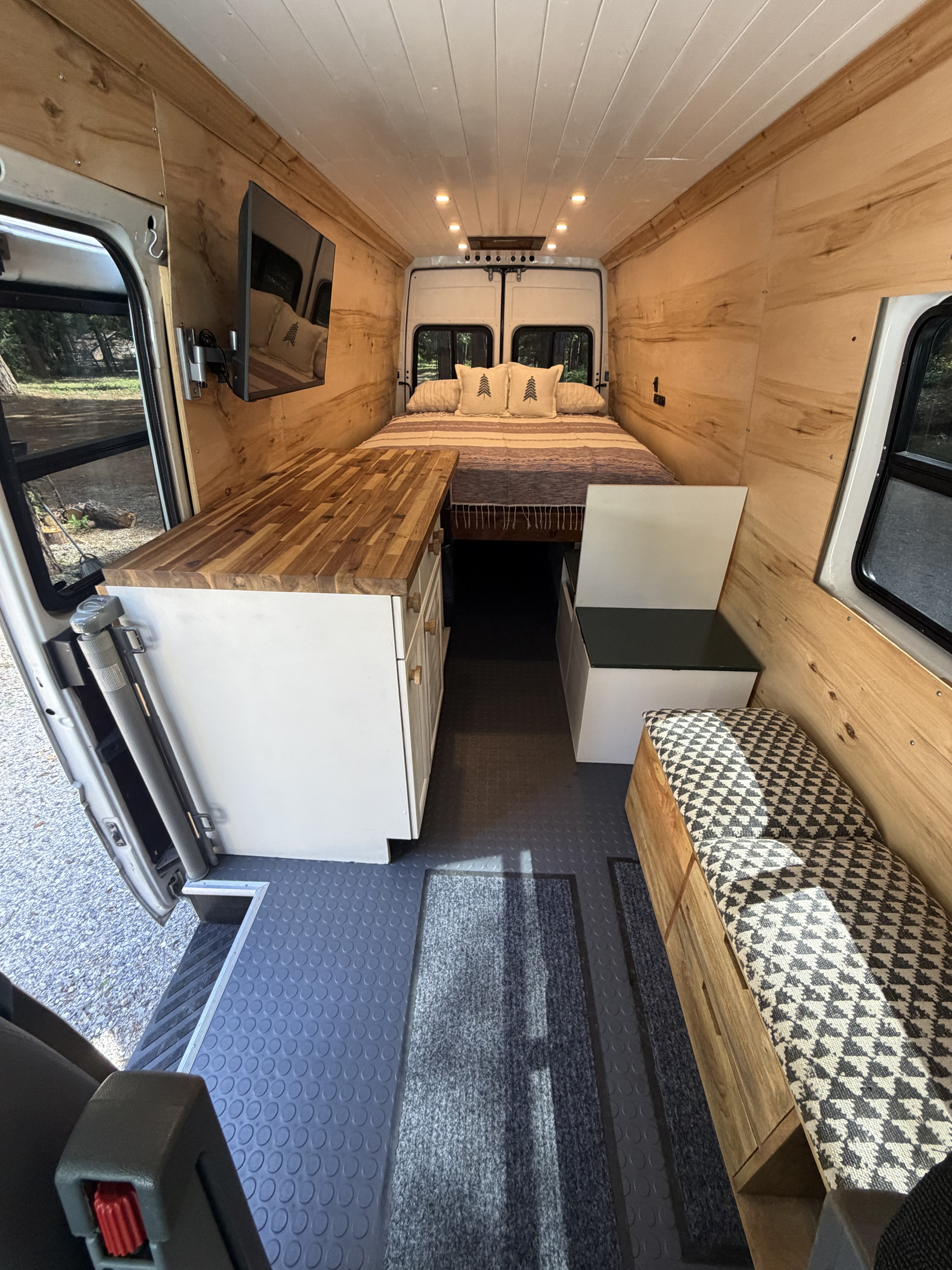 Interior of a stylish rv rental camper van. Features a bed, wooden walls, kitchen counter, and seating area.. Dodge Sprinter 2500 170ext 2005