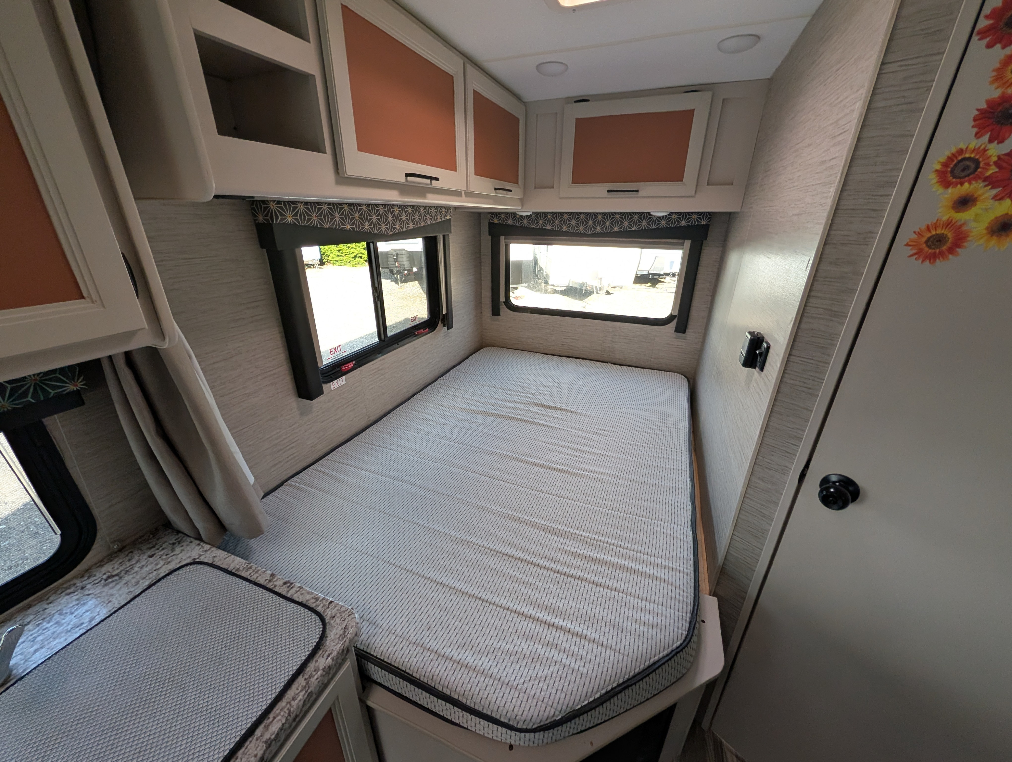 RV rental bedroom: a cozy space with striped mattress, windows, overhead cabinets, and patterned valances.. Thor Freedom Elite 2022