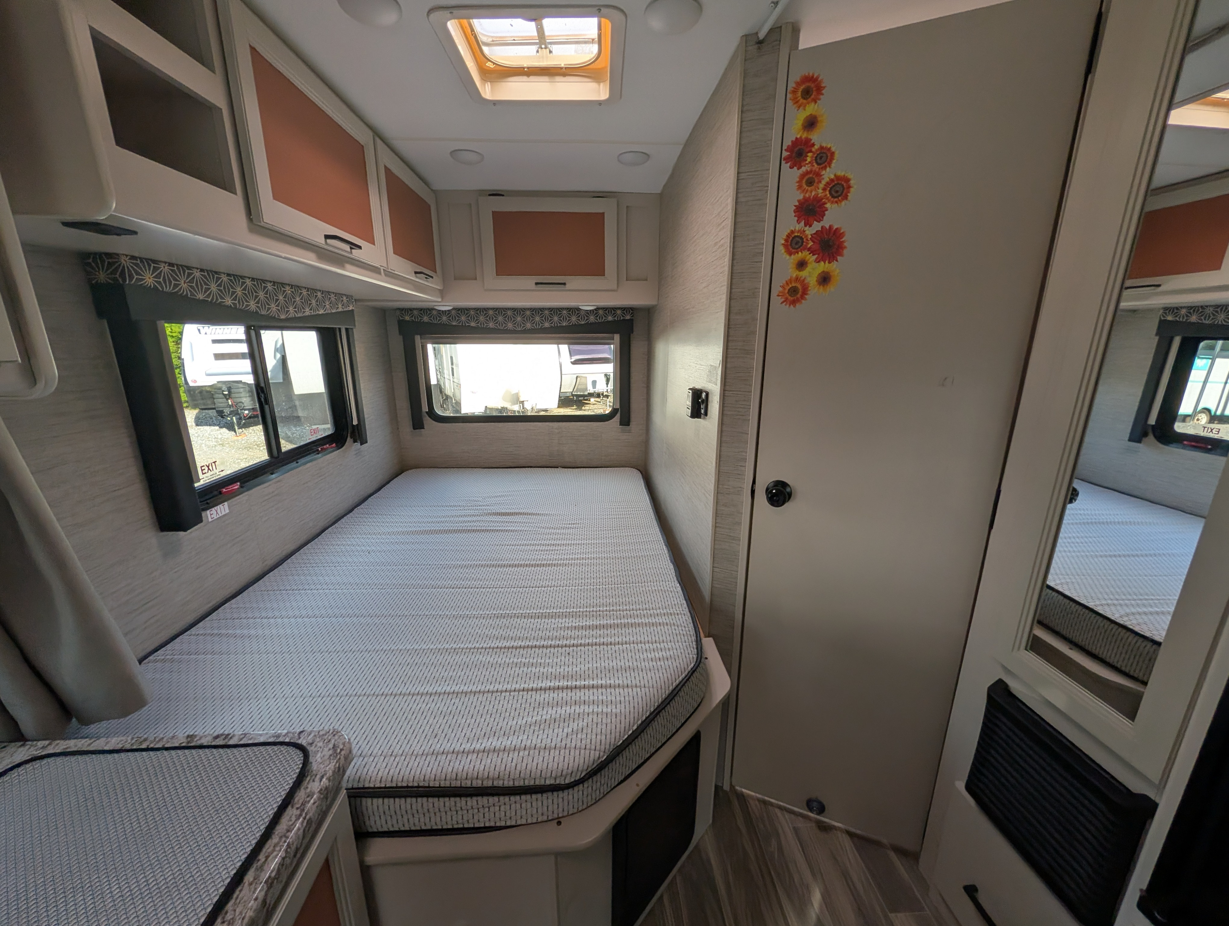Cozy RV rental bedroom featuring a large bed, overhead cabinets, windows, a skylight, and a door with sunflower decals.. Thor Freedom Elite 2022