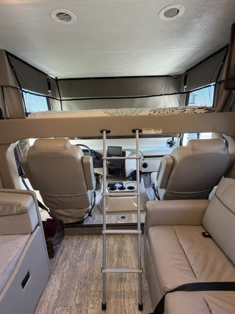 Inside an RV rental: a spacious interior with an overhead bunk bed, safety net, ladder, front swivel seats, and a comfortable sofa.. Thor Hurricane 2020