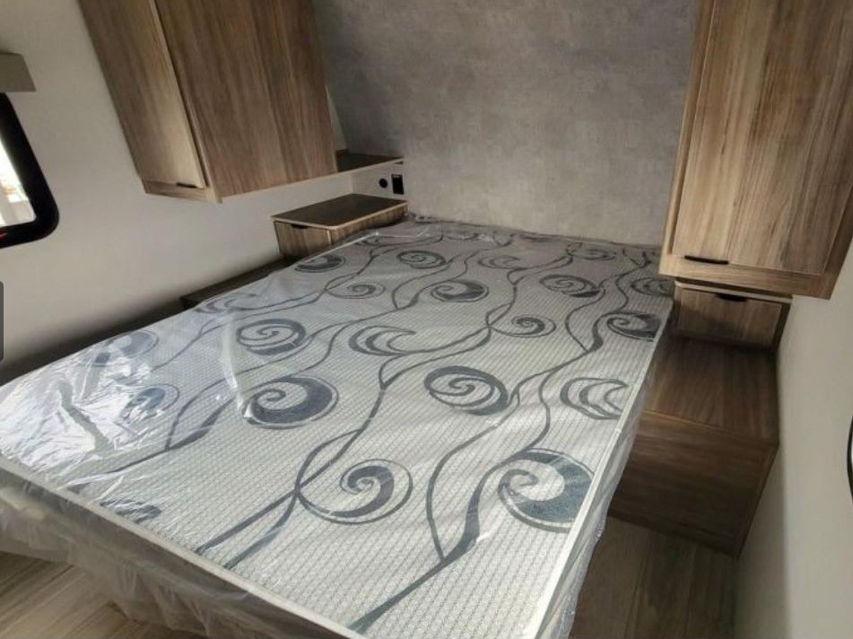 RV rental bedroom featuring a new, plastic-wrapped mattress, built-in overhead cabinets, and integrated side tables.. Winnebago Access 2025