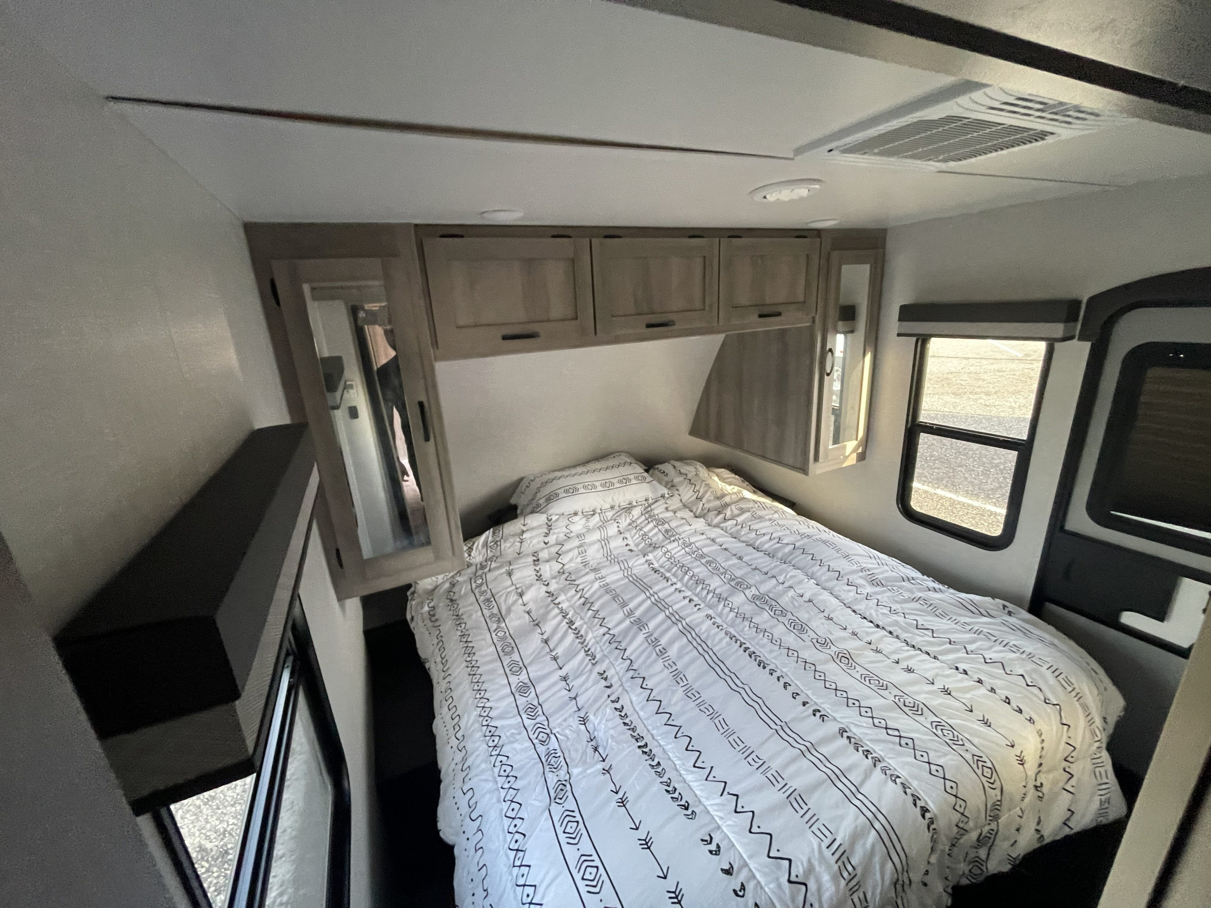 Modern RV rental bedroom with a comfy patterned bed, overhead storage, mirrored closets, a window, and ceiling AC.. Winnebago Voyage 2021