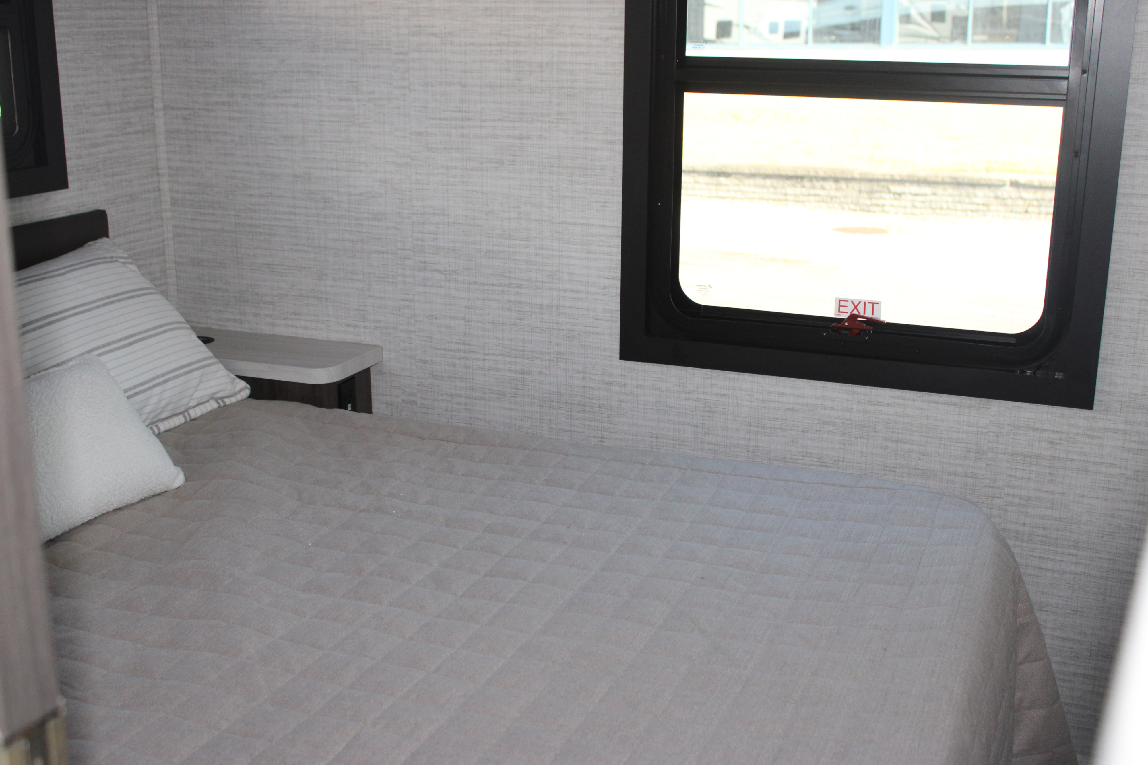 Inside an rv rental, a comfortable bedroom area features a quilted bed, pillows, and a window with an emergency exit sign.. Jayco Greyhawk 2025