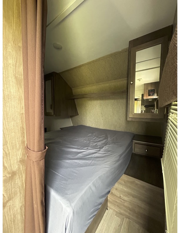 Compact rv rental bedroom: bed with gray sheet, mirrored cabinet, storage shelf, and window blinds.. Dutchmen Coleman Lantern 2019