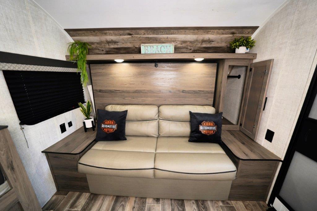 RV rental interior: A compact living space featuring a comfy sofa-bed, rustic wood paneling, and built-in storage.. Gulf Stream Ameri-Lite Super Lite 2023