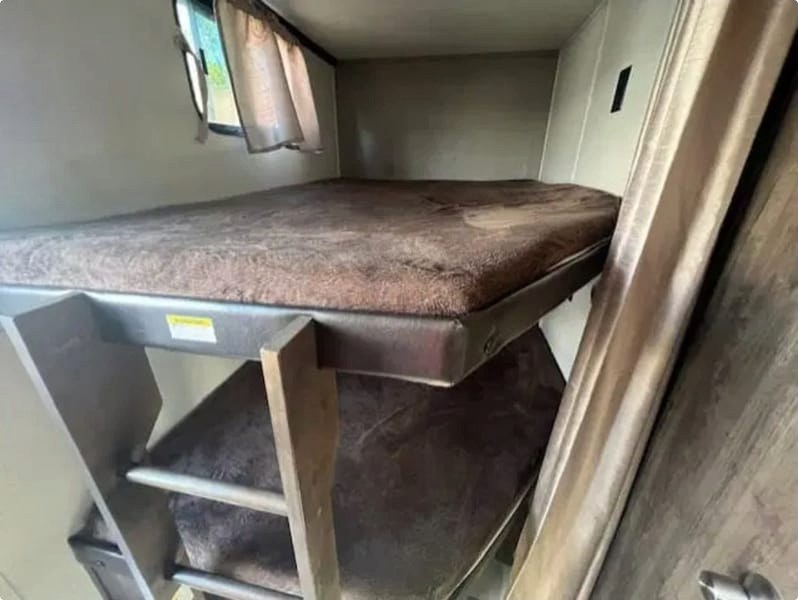 Cozy RV rental bunk beds with brown mattresses and a window, ideal for extra sleeping space on your adventure.. Crossroads RV Volante 2019