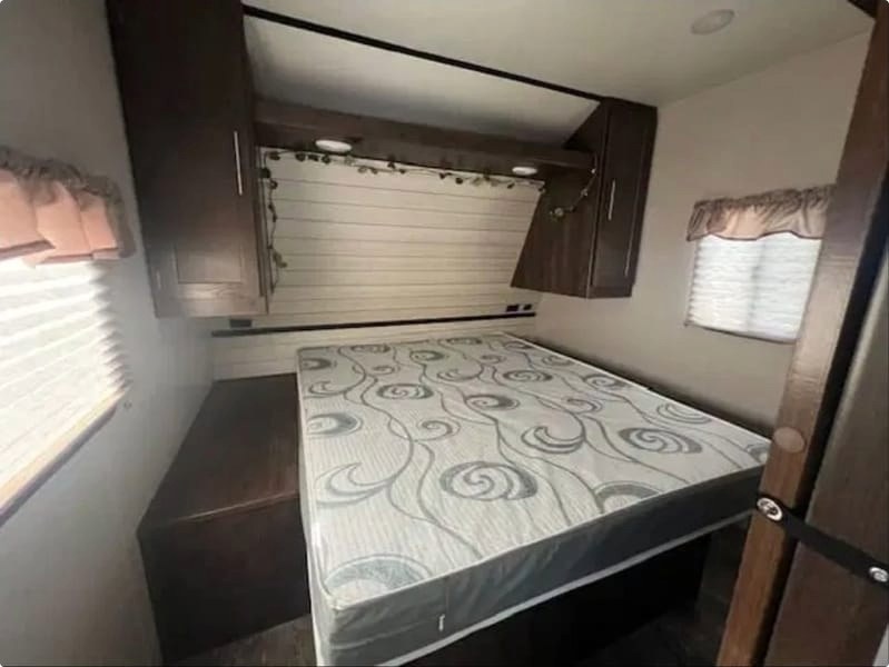 **RV rental** bedroom features a patterned mattress, overhead storage cabinets, and a window with blinds. Ideal for travel.. Crossroads RV Volante 2019