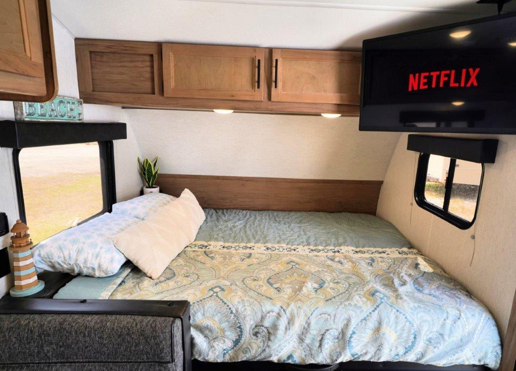 RV rental bedroom interior: cozy bed with paisley bedding, wall-mounted Netflix TV, wood cabinets, and windows with decor.. Forest River Cherokee Wolf Pup 2023