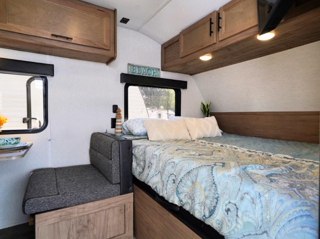 Relax in this cozy RV rental bedroom featuring a bed with paisley bedding, storage, a bench, and a beachy vibe.. Forest River Cherokee Wolf Pup 2023