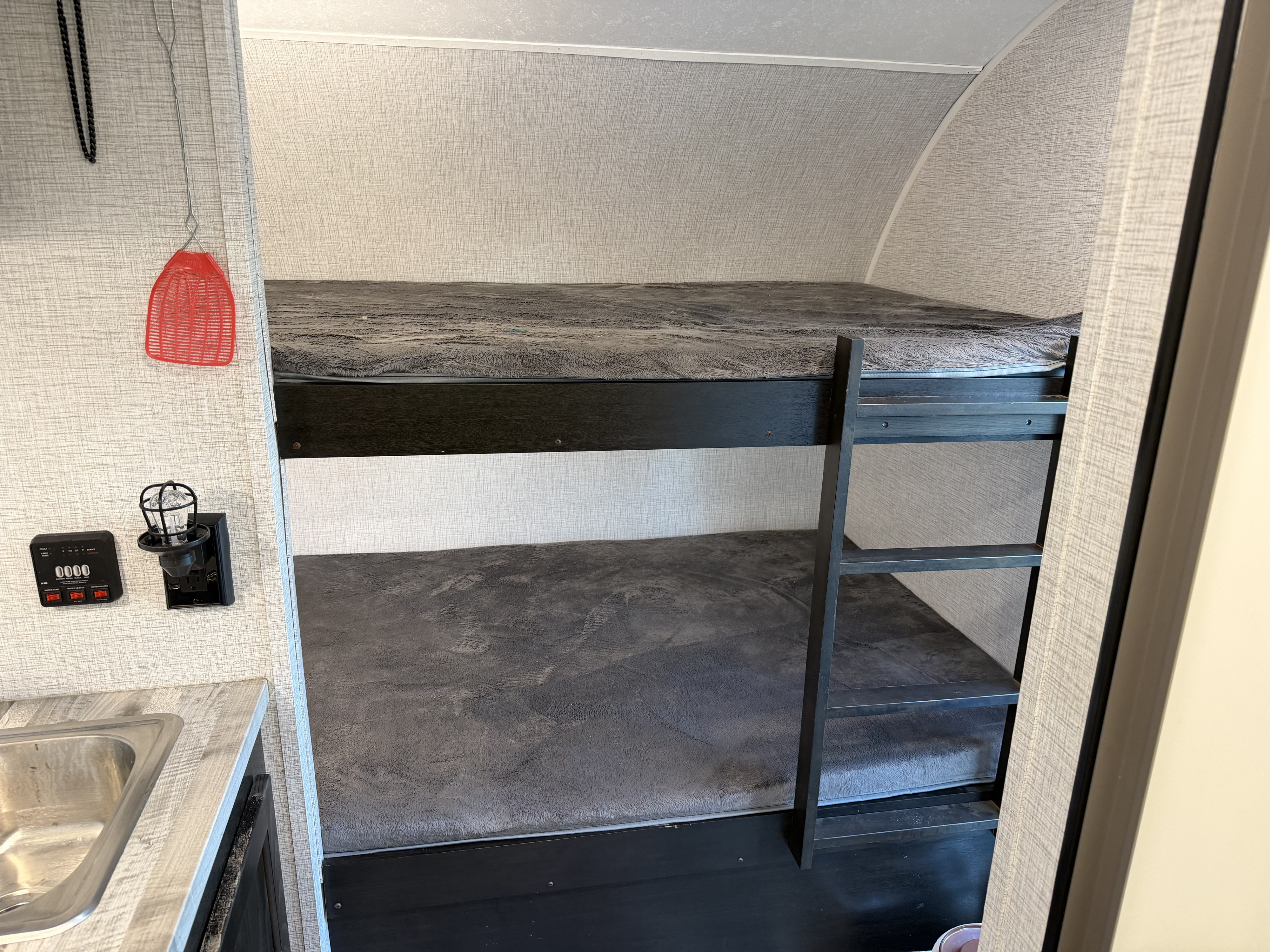 Inside this RV rental are dark bunk beds with cozy grey blankets, a ladder, a small sink, and a control panel with a light.. Braxton Creek Free Solo 2021